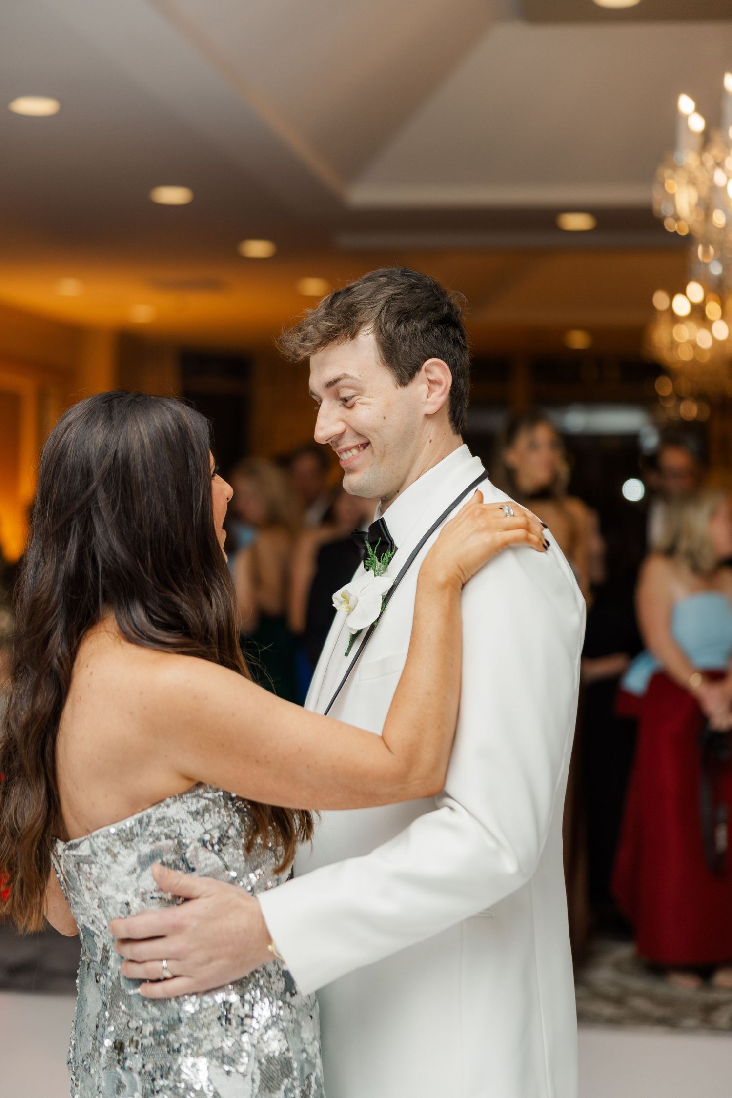 A couple shares an intimate dance at their wedding reception under warm lighting and chandeliers.