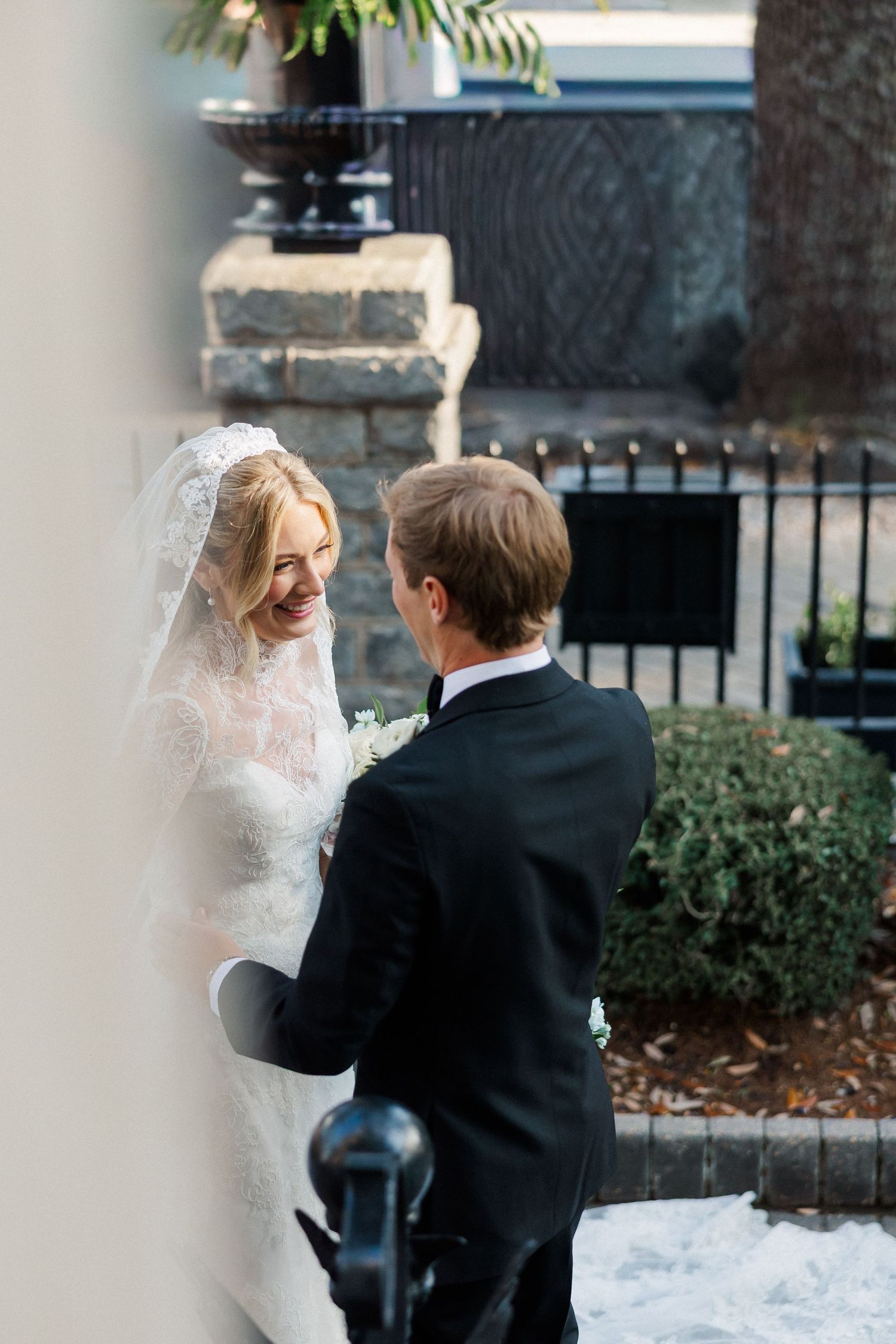 A romantic wedding moment captured outdoors with a beautiful lace veil and classic black tuxedo.
