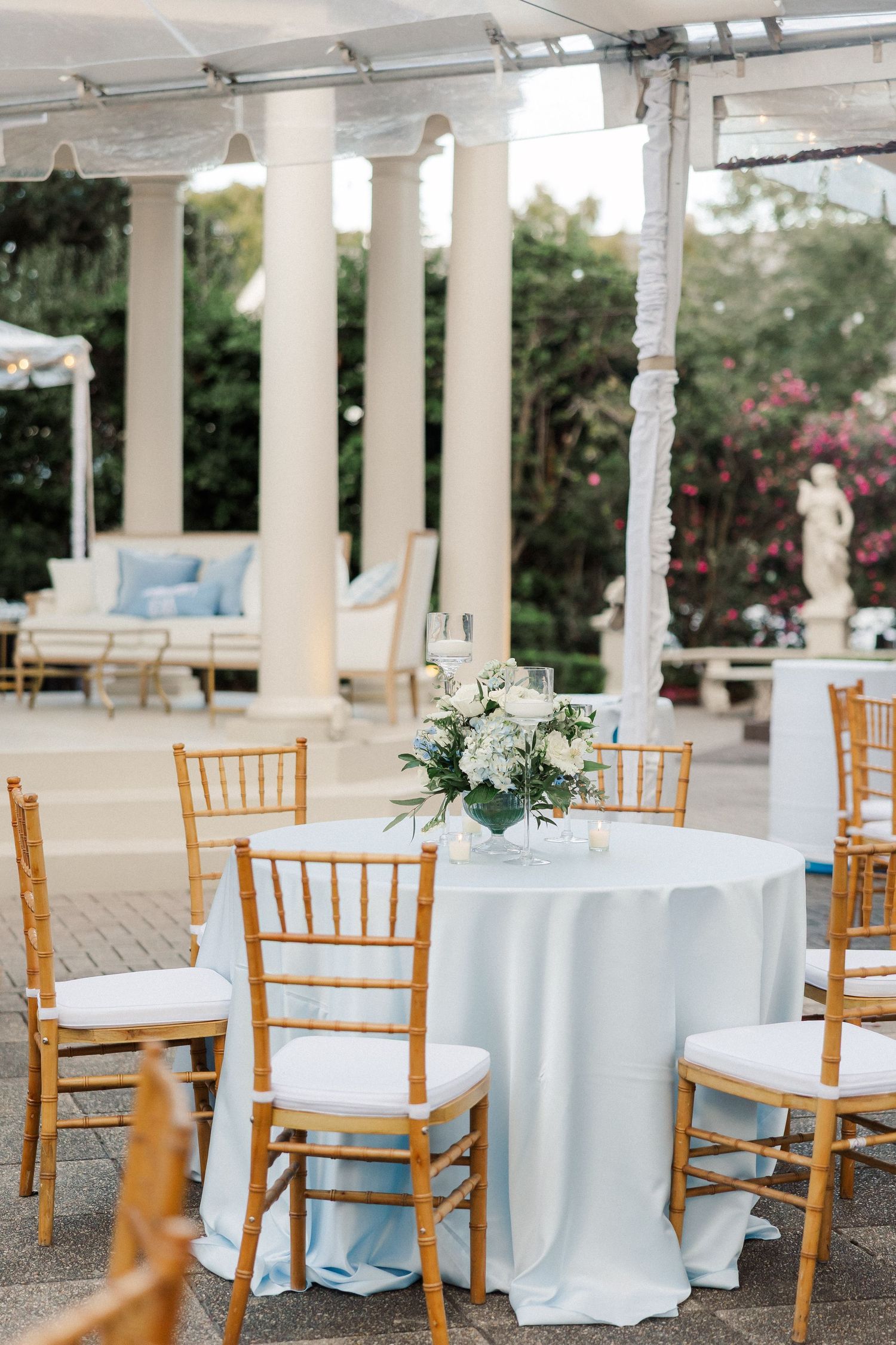 Elegant outdoor wedding reception setup with white linens, chiavari chairs and floral centerpieces.