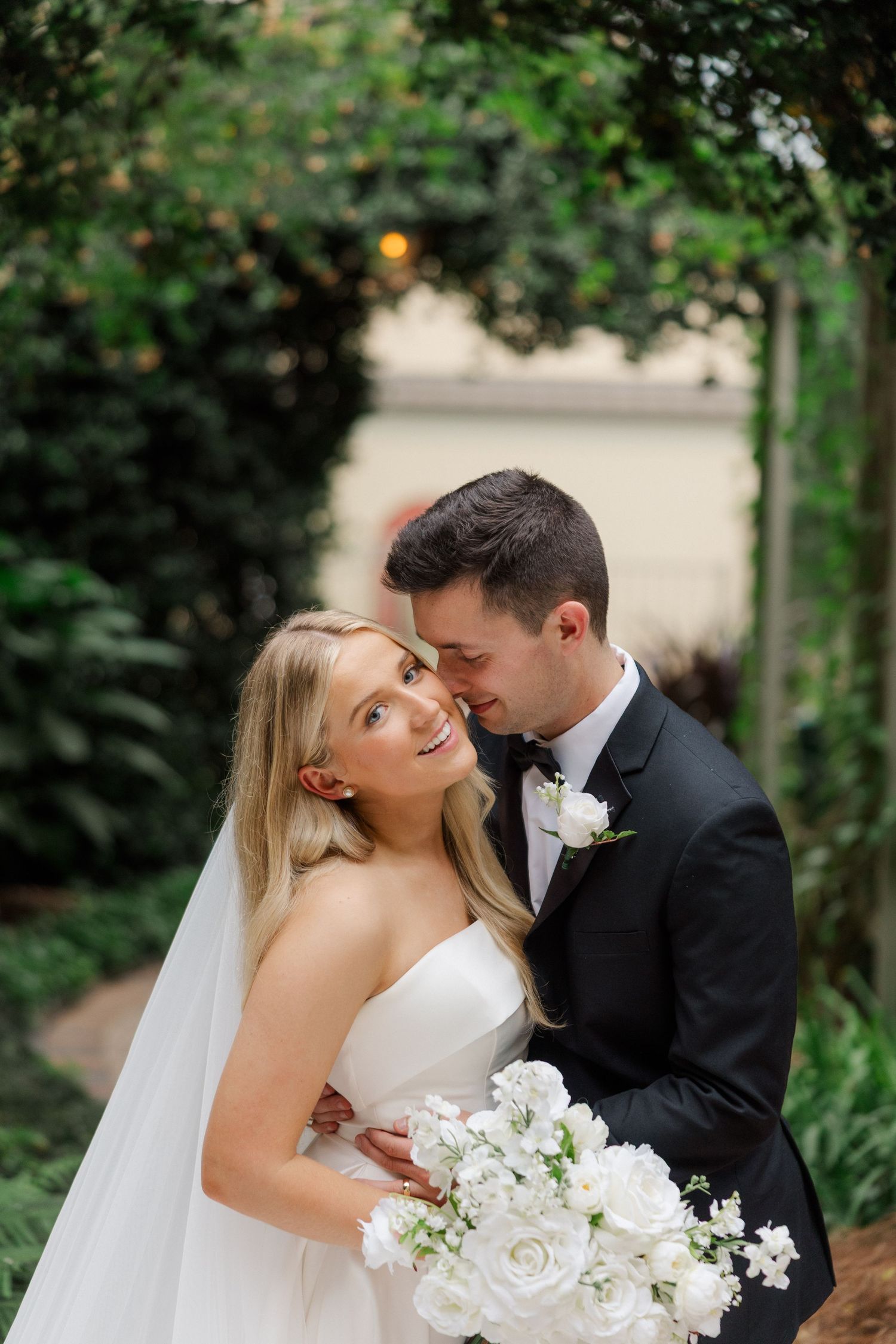 Romantic wedding couple embracing in a garden setting with white floral bouquet.