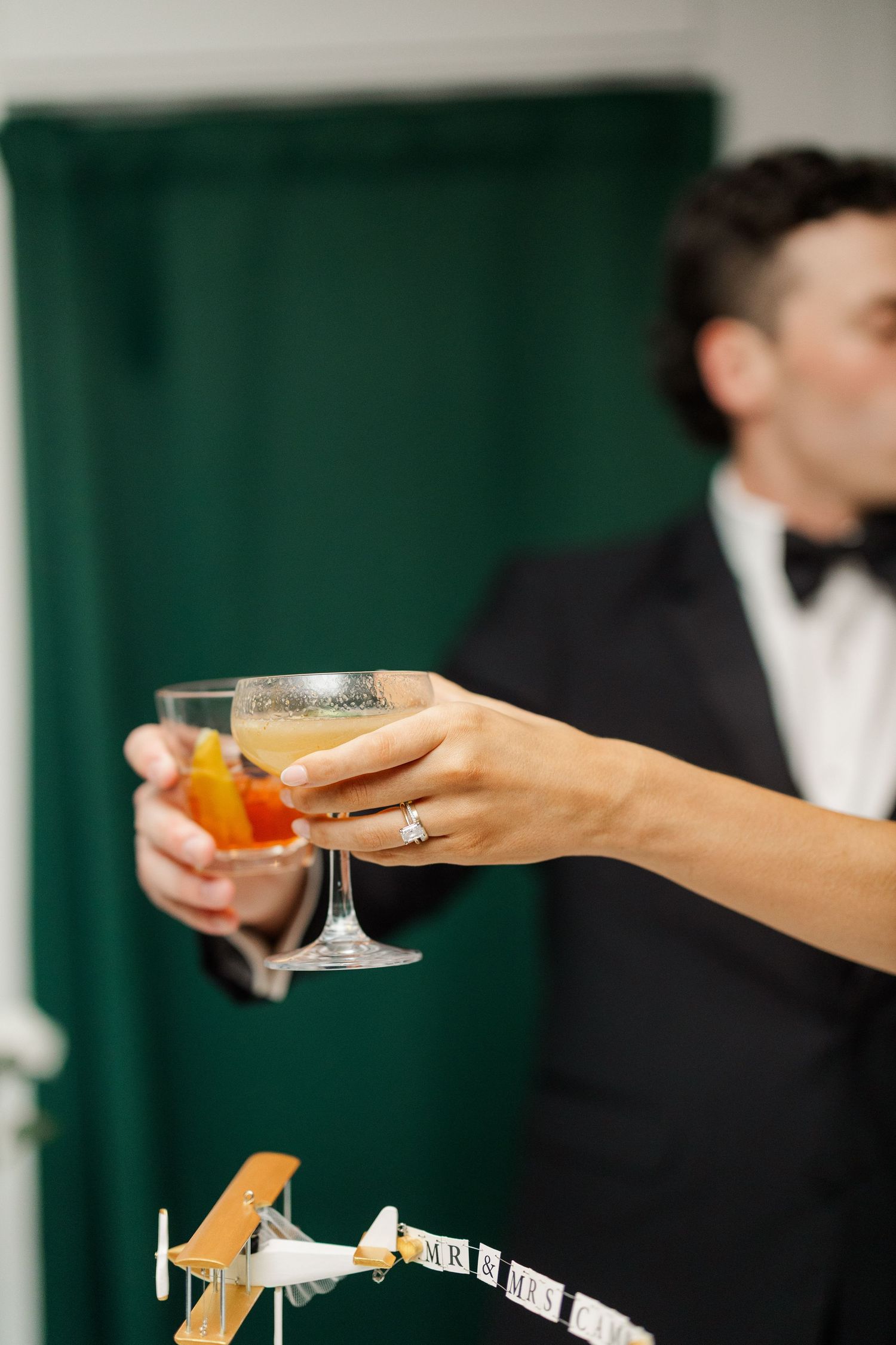 Wedding reception detail showing hands holding champagne glasses against an elegant dark green backdrop.