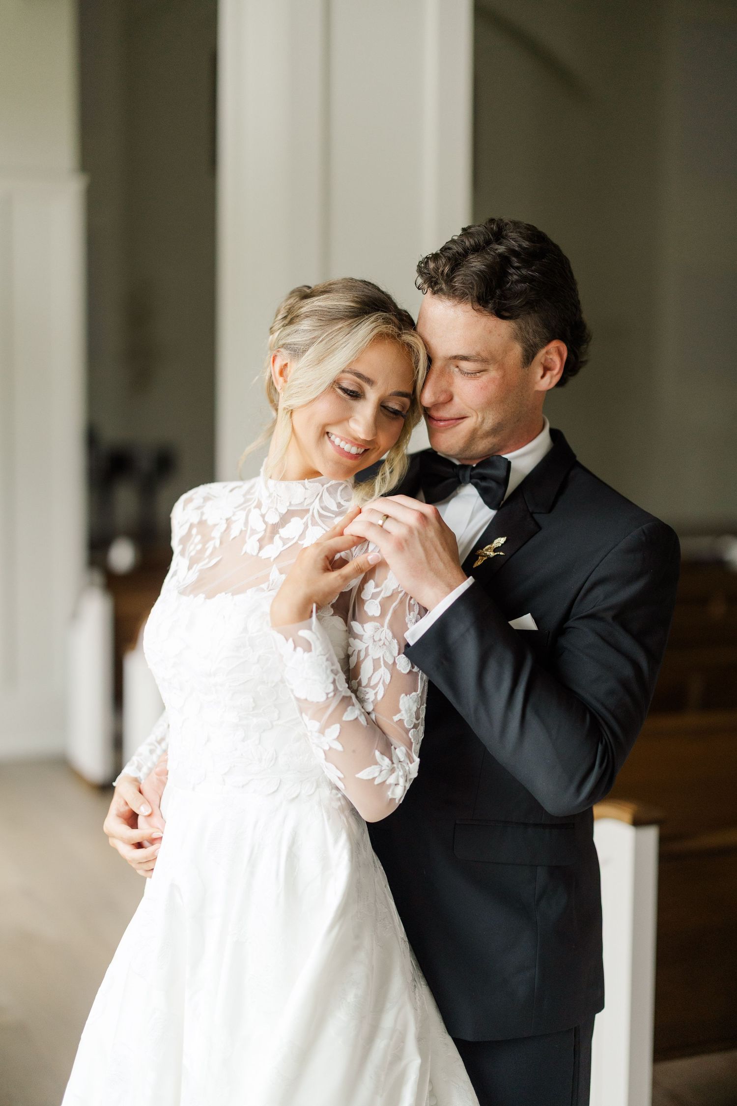 Tender embrace between bride in lace gown and groom during wedding day first look.