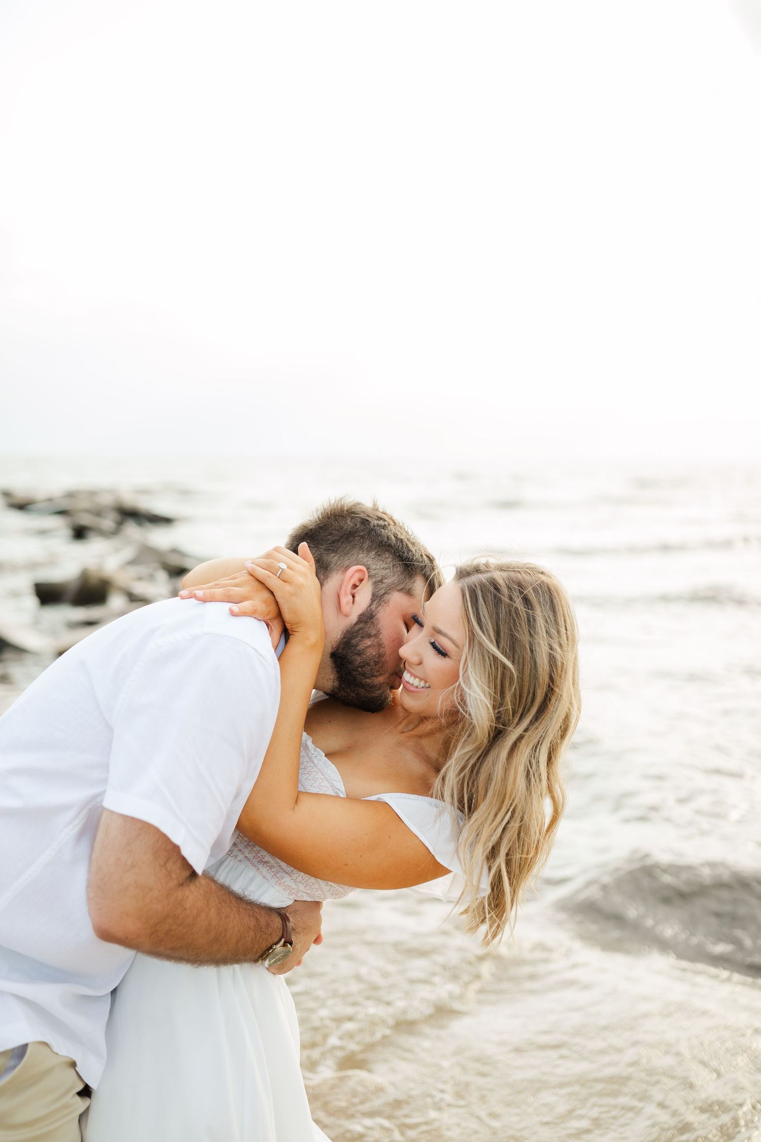 A romantic couple shares an intimate moment embracing on a rocky beach at sunset.