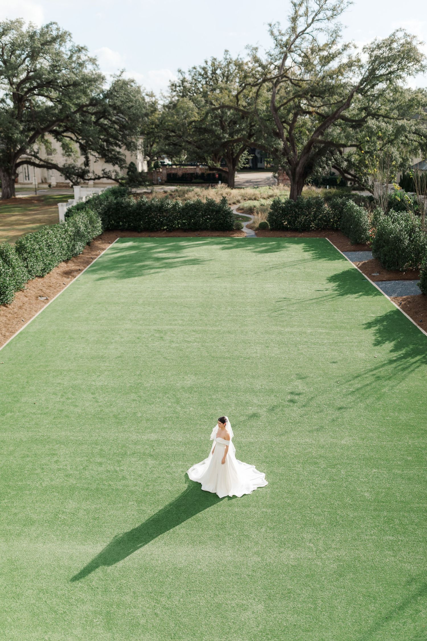 A bride on a manicured green lawn creates a striking silhouette against the landscaped garden setting.