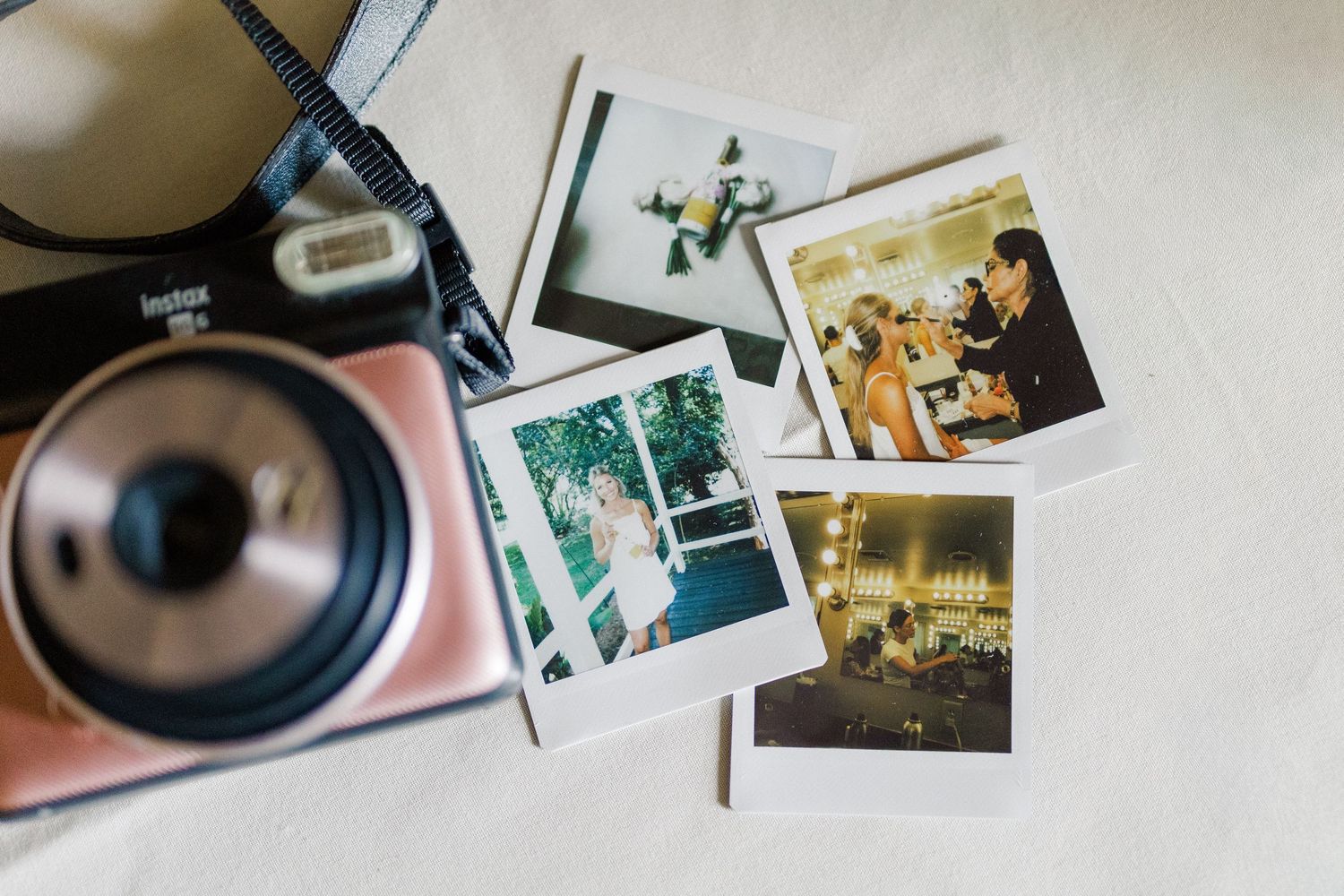 Fujifilm Instax Mini camera beside four polaroid photos showing wedding and event moments on a white surface.