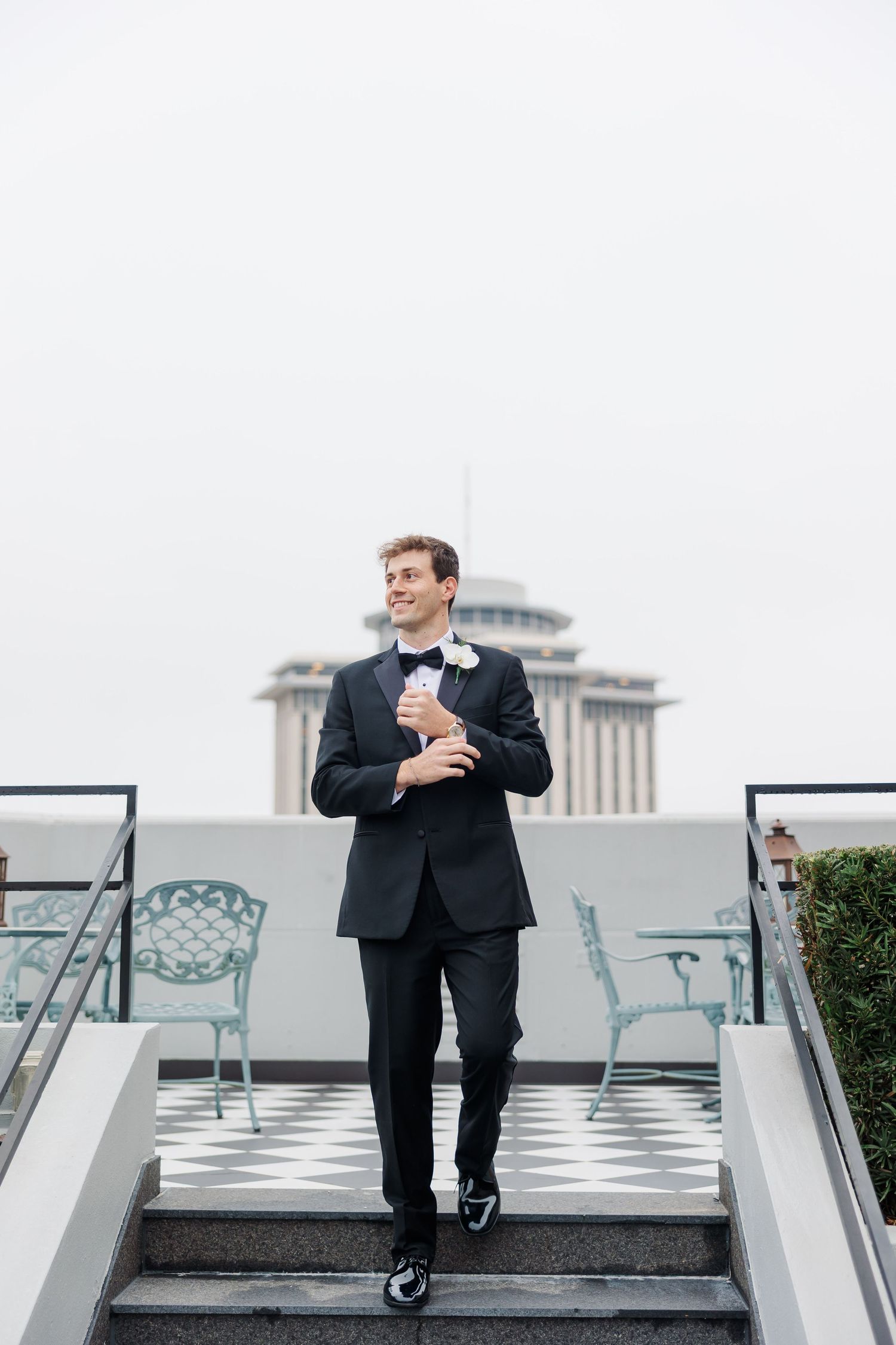 Man in formal attire sitting on outdoor steps with cityscape in background.