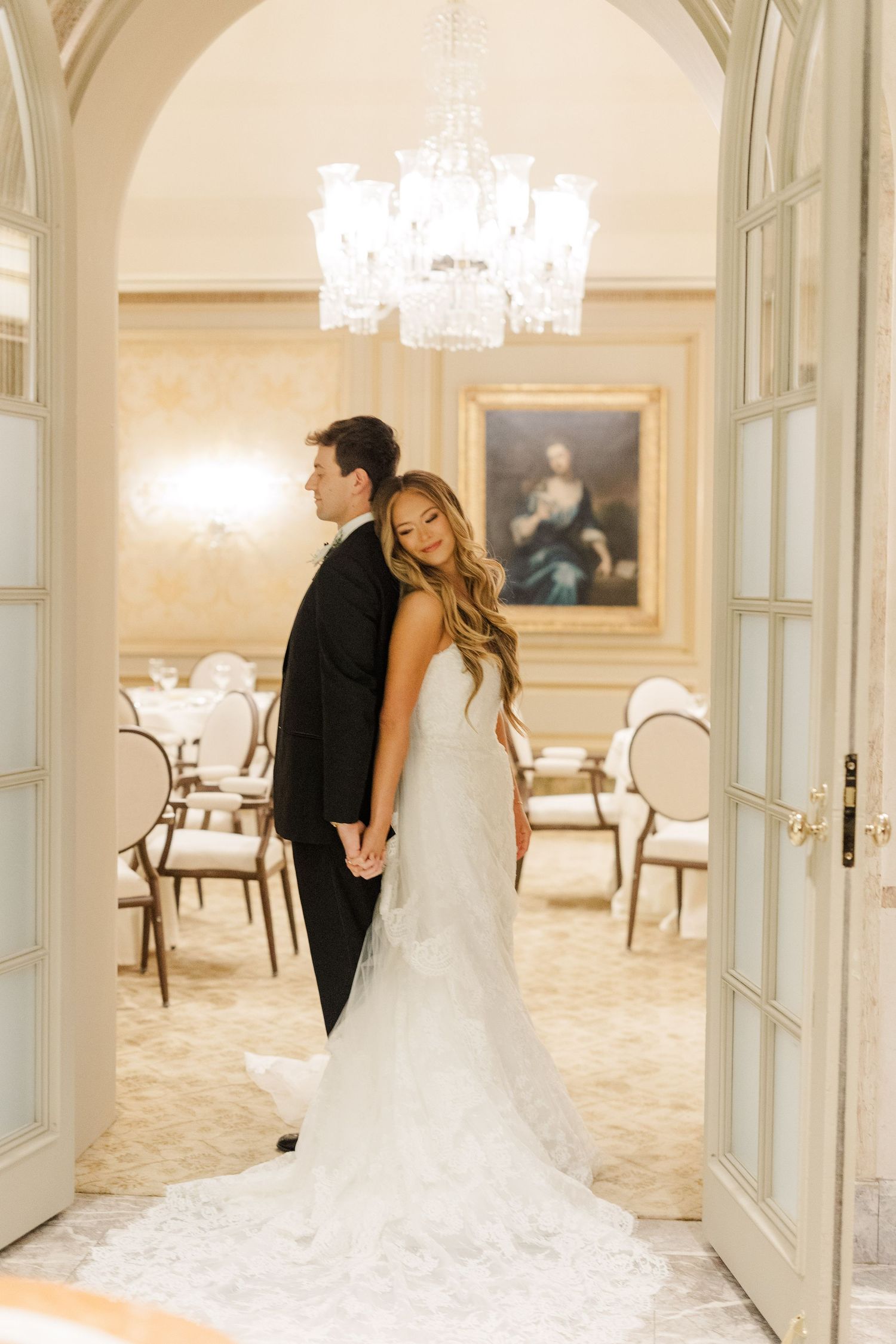 Romantic wedding photo in an elegant room with chandelier and white French doors.