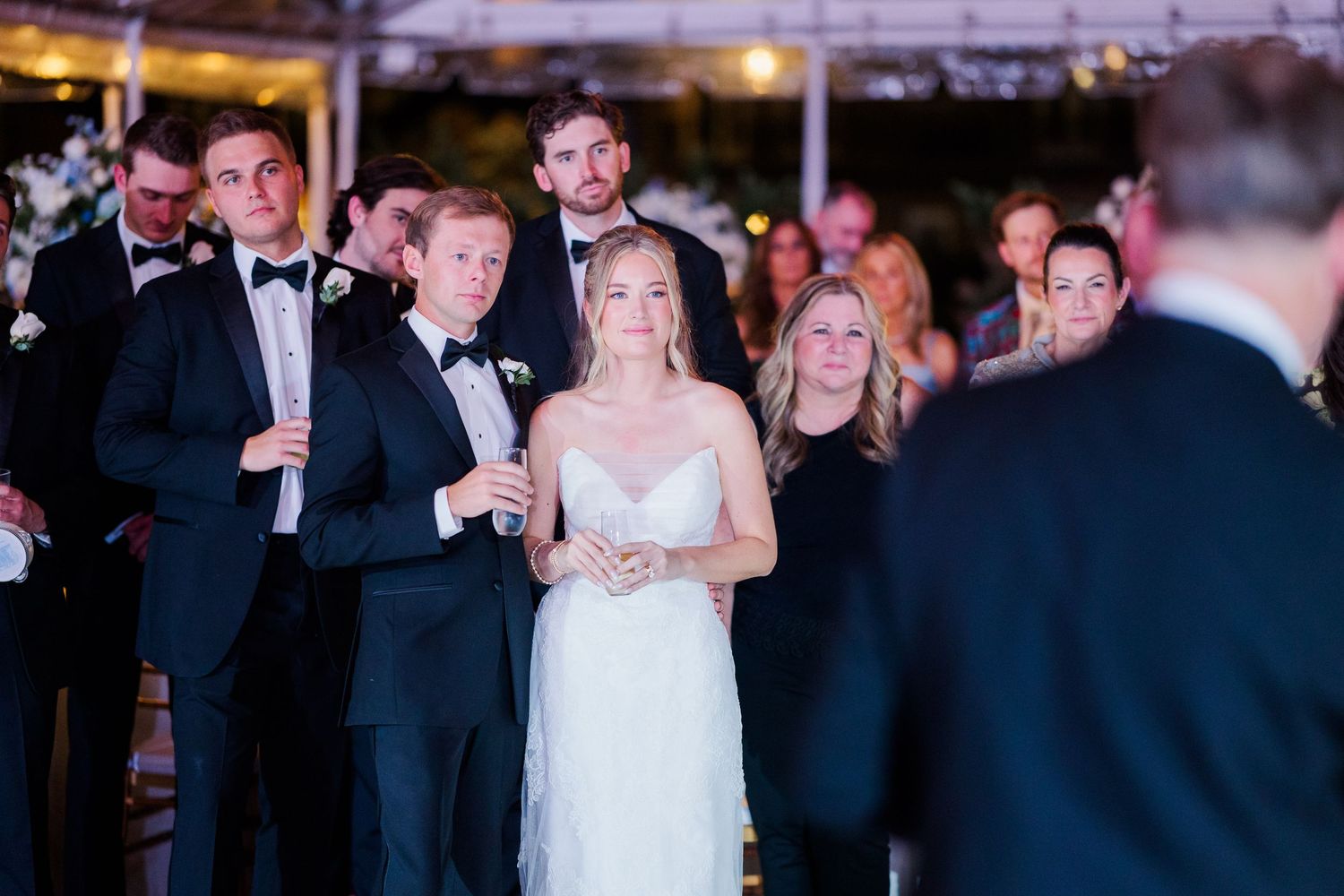 Wedding reception crowd gathered in formal attire under dim lighting.