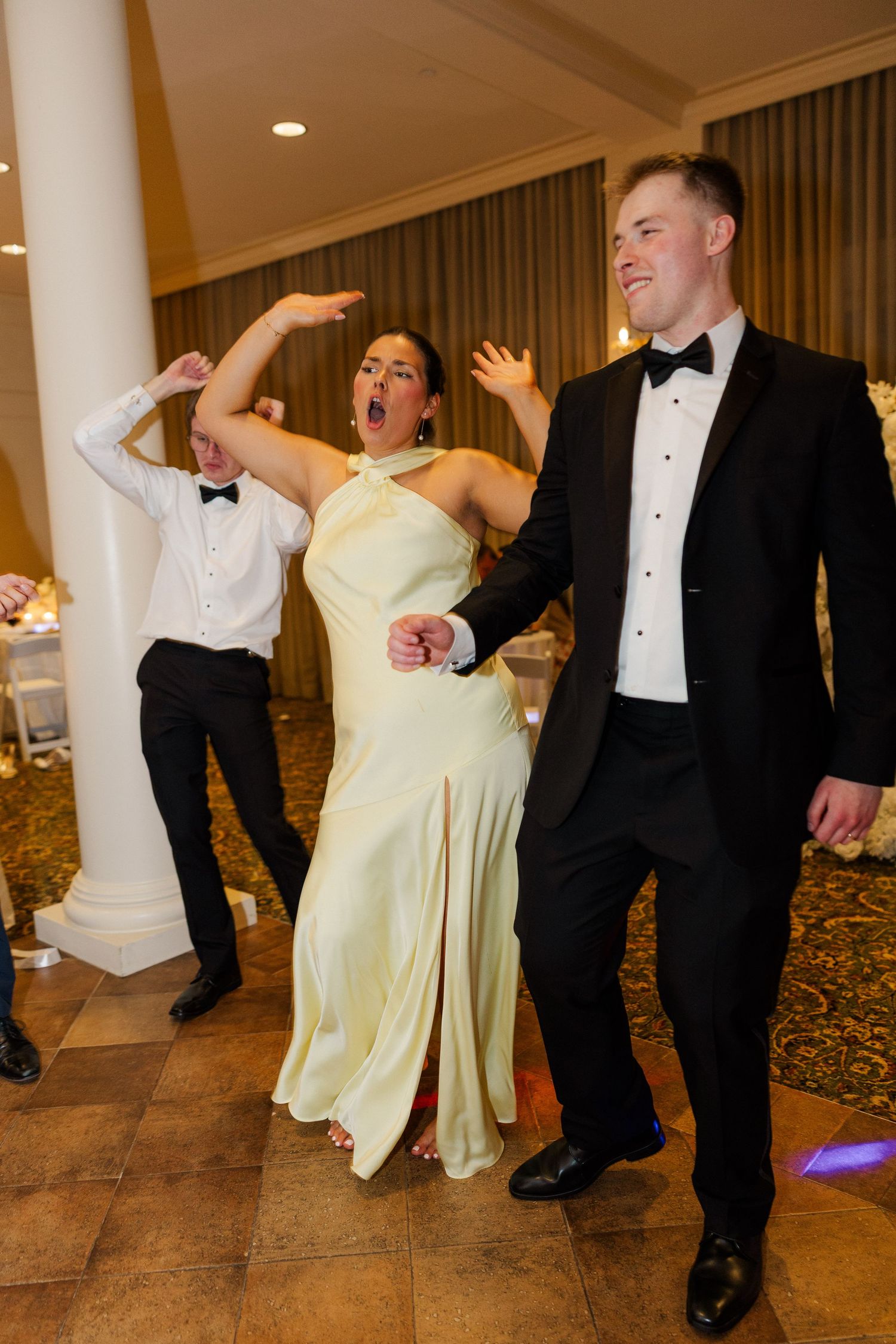 Wedding guests in formal attire dance energetically at an elegant reception venue.