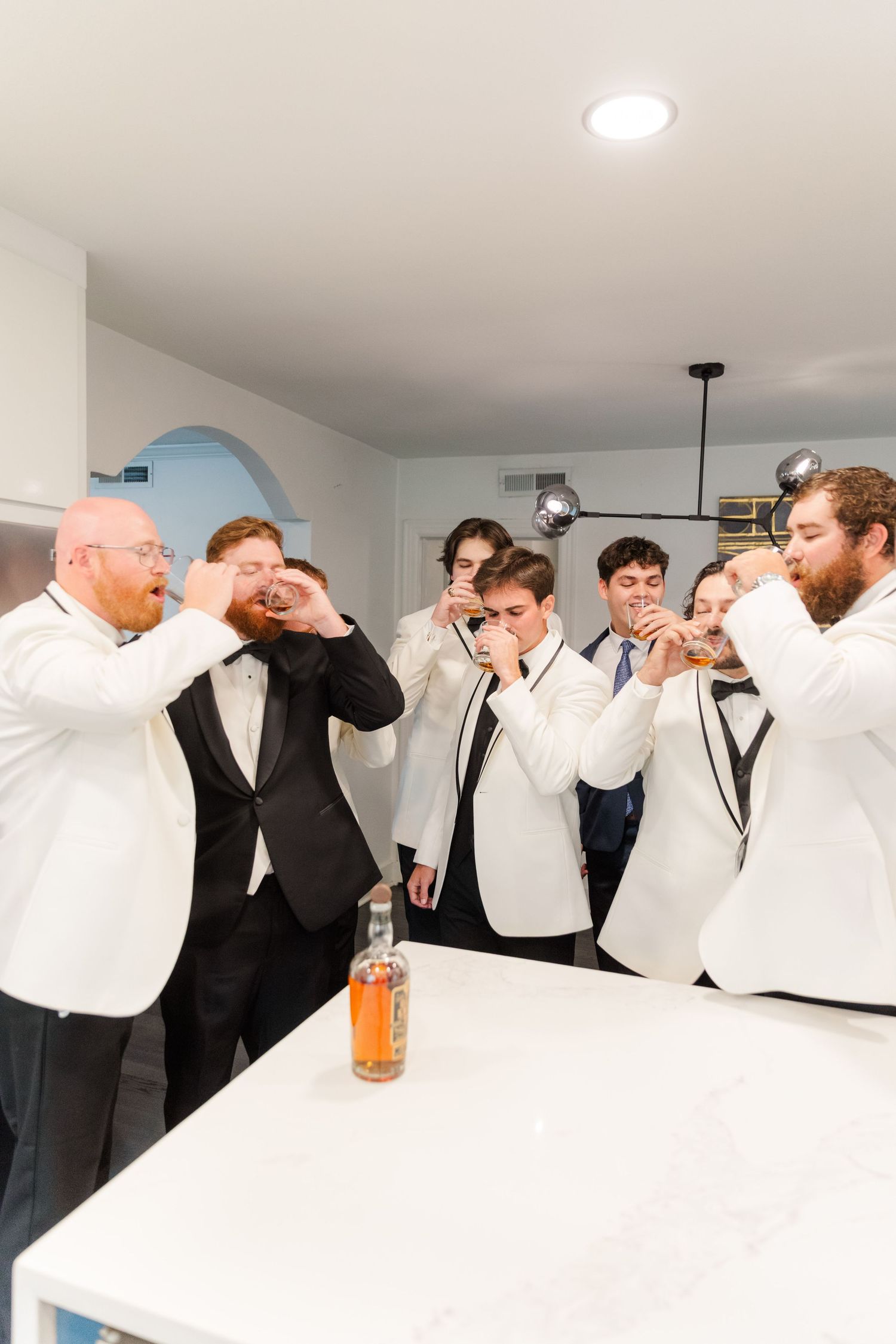 Group in white dress shirts and dark suits taking celebratory drinks together at wedding event.