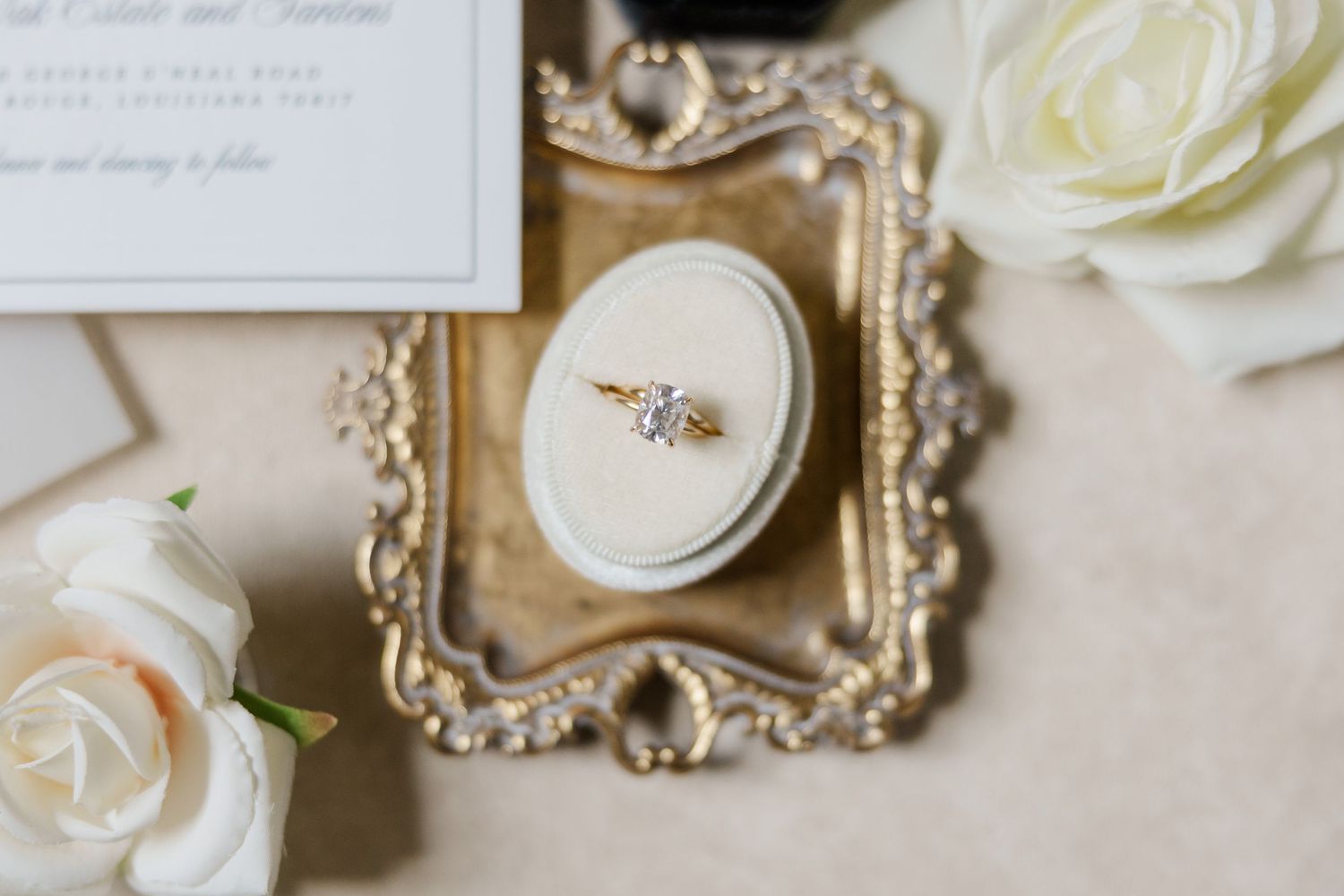 Elegant wedding details including white roses, vintage frames, and delicate jewelry arranged on a cream colored surface.