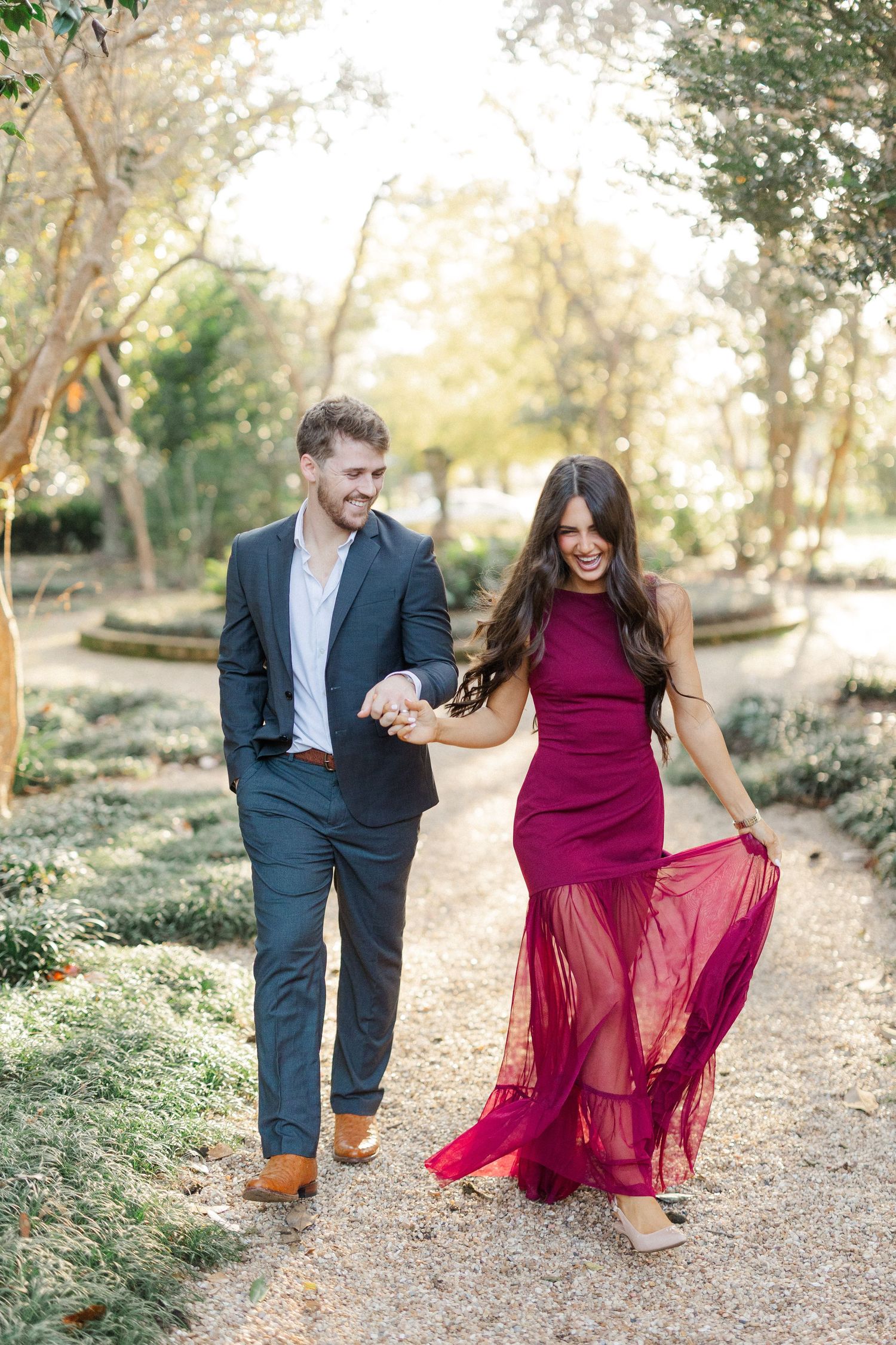 Couple walks together on garden path with woman in flowing burgundy dress twirling.