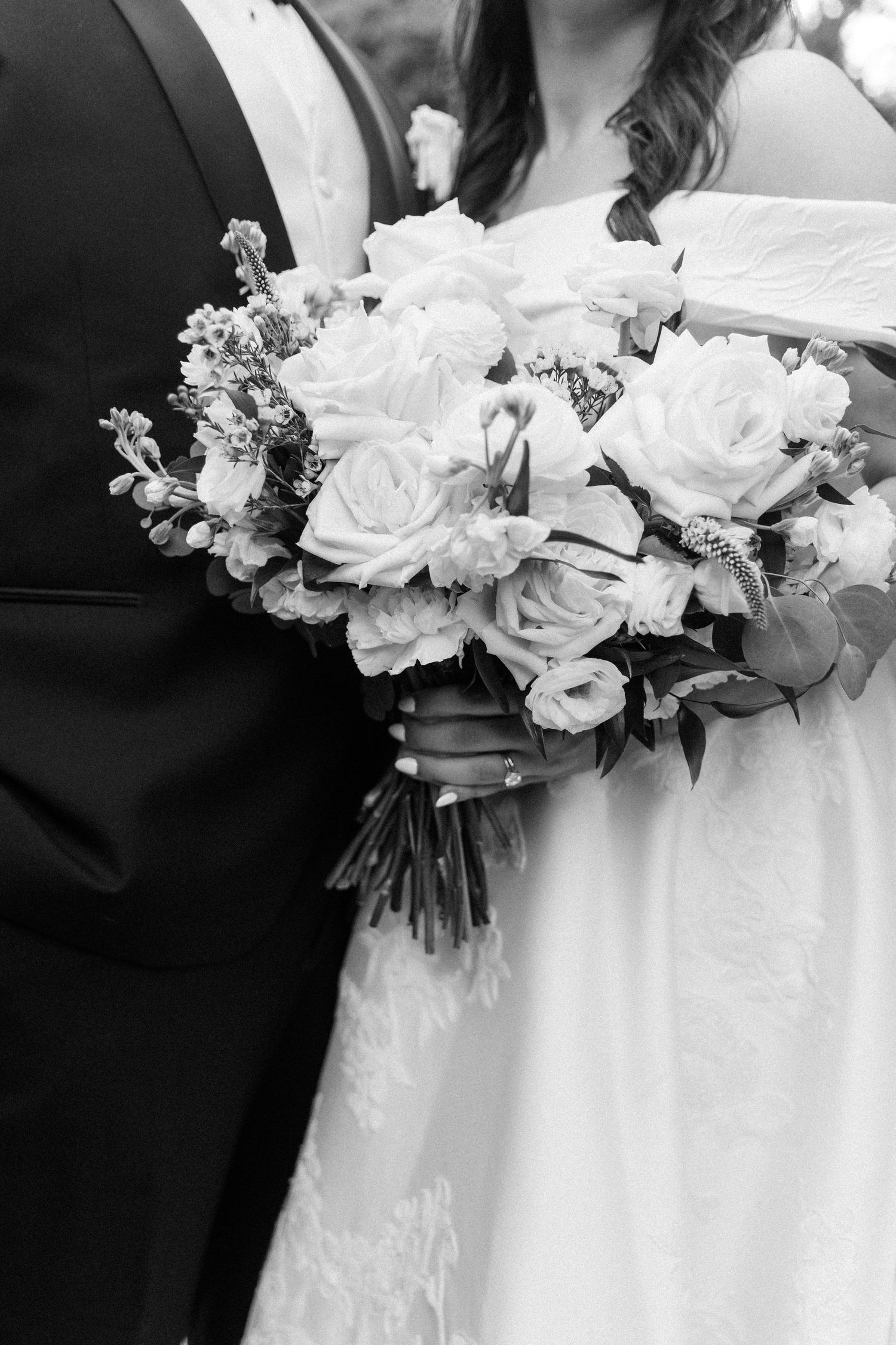 Close-up of an elegant white rose wedding bouquet held against formal attire.