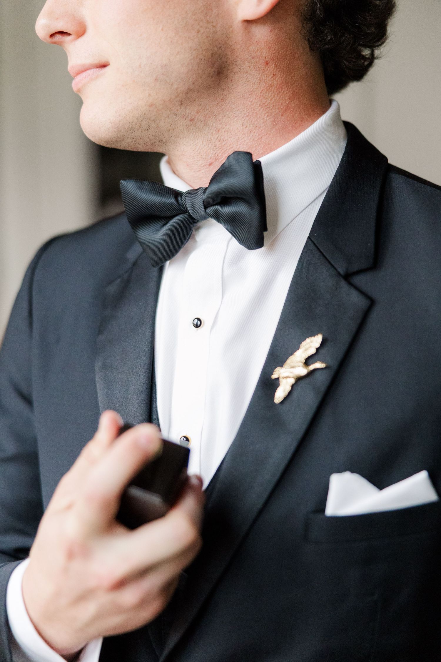 Close-up details of a groom adjusting his black bow tie and formal attire.
