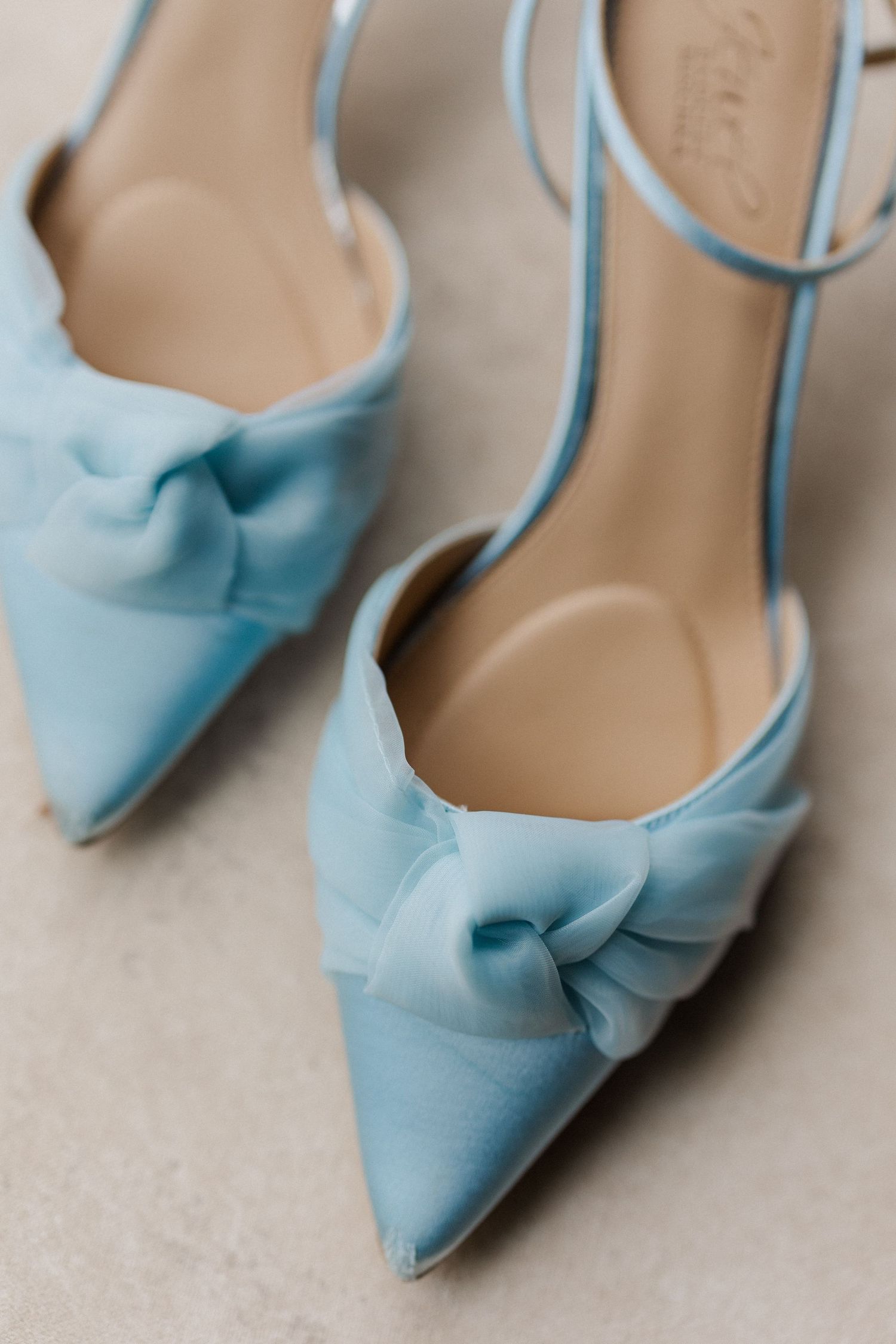 Light blue satin bridal shoes with decorative bows displayed in a row.