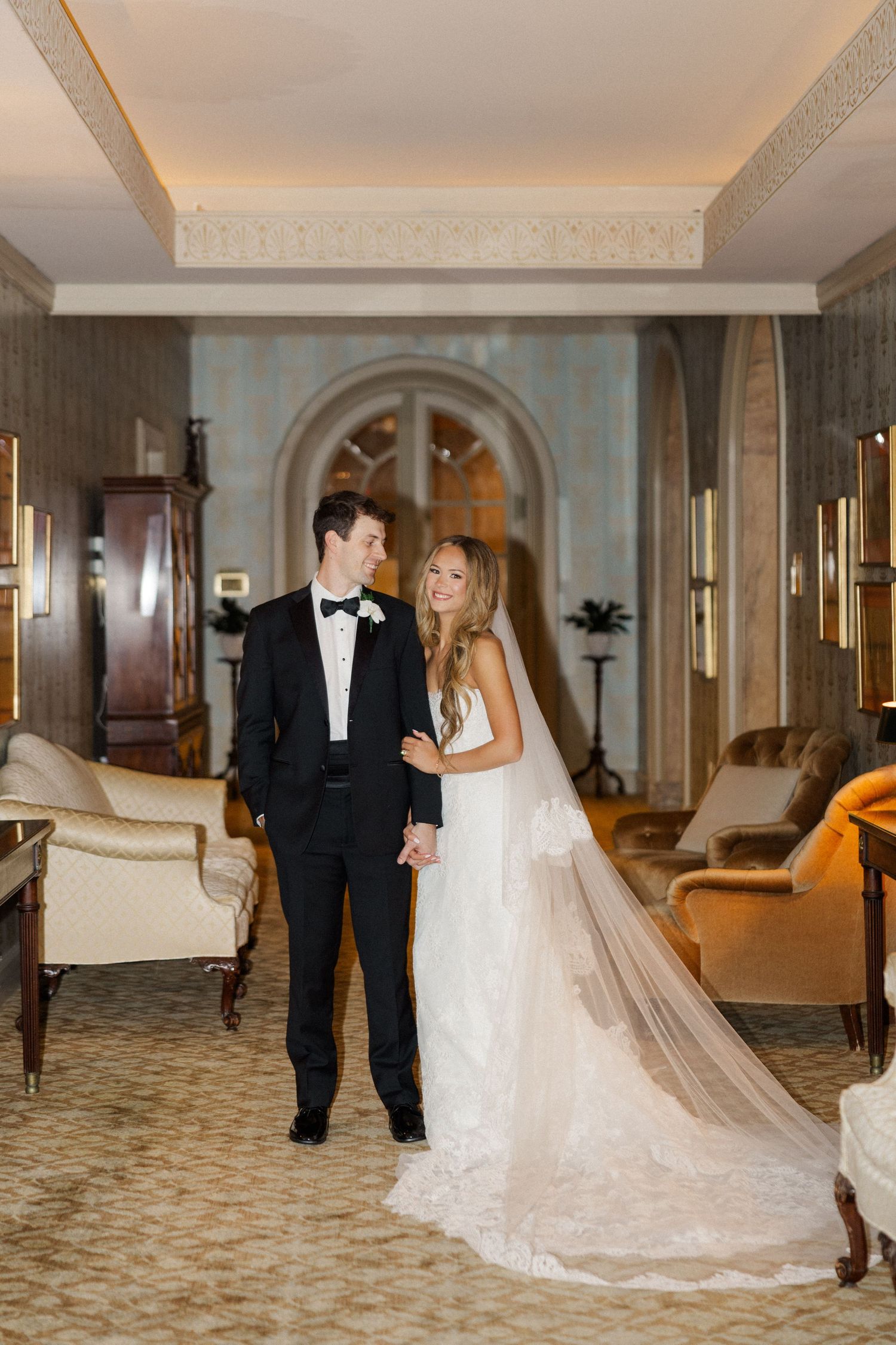 Wedding couple sharing intimate moment in luxurious hotel corridor with ornate decor.