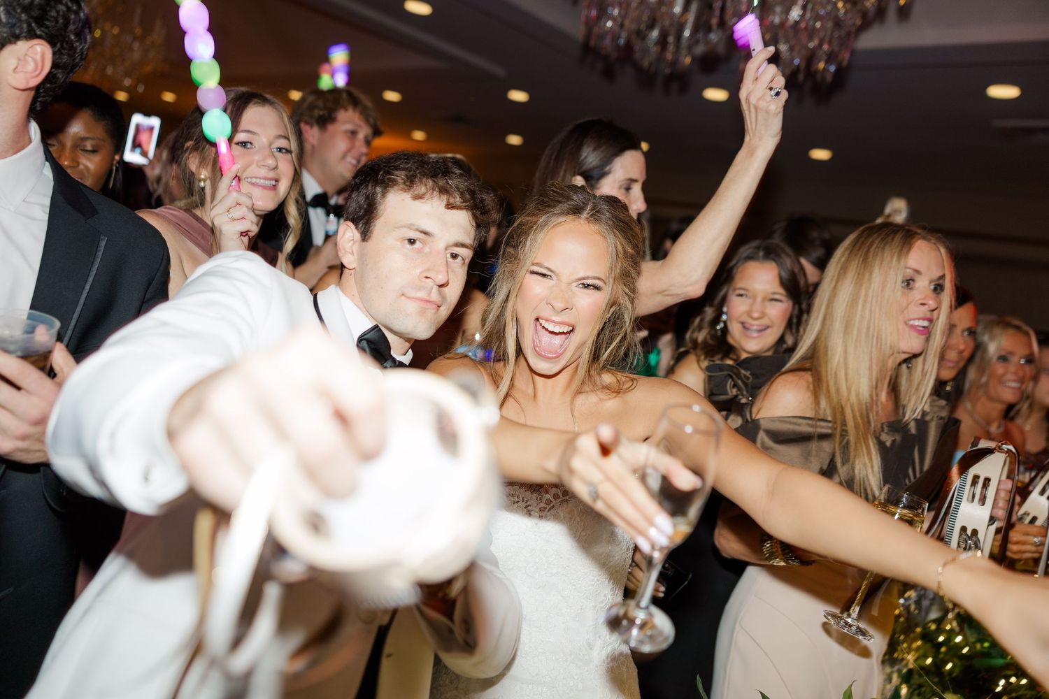 Wedding celebration with guests dancing and celebrating with drinks at a lively reception party.