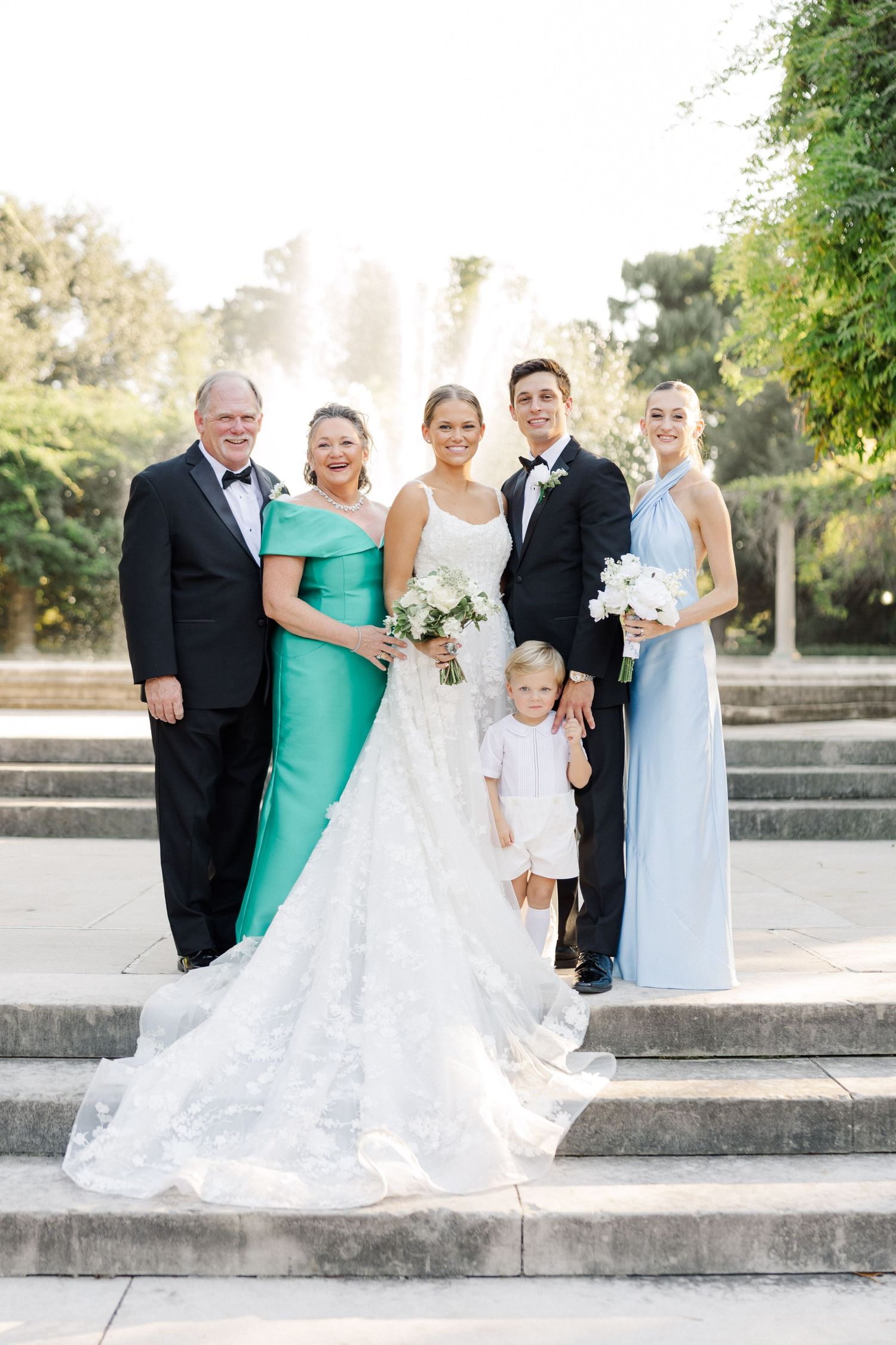Wedding party poses on stone steps in formal attire with bridesmaids in light blue and one guest in teal.
