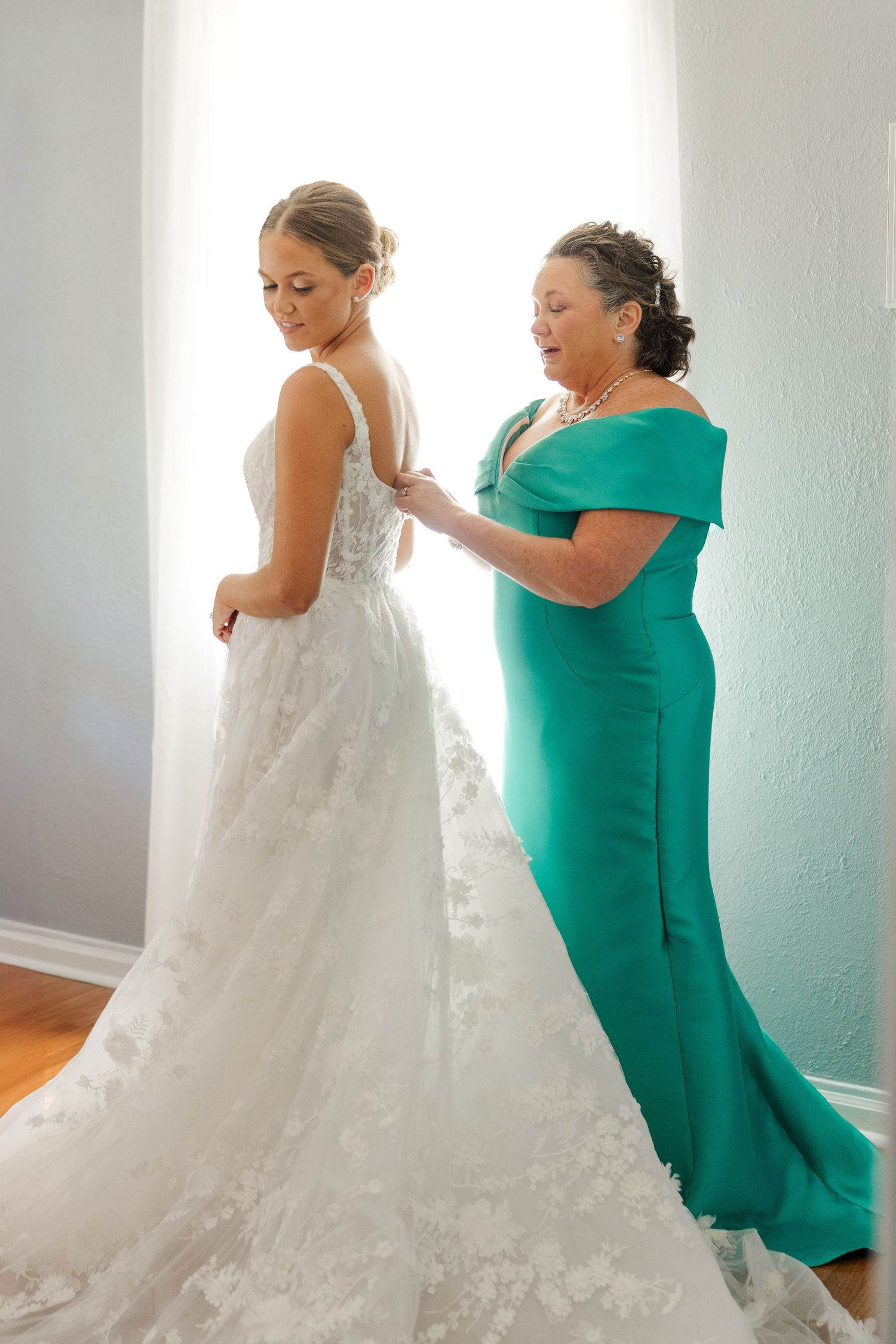 Someone in a green dress helps adjust a flowing white wedding gown.