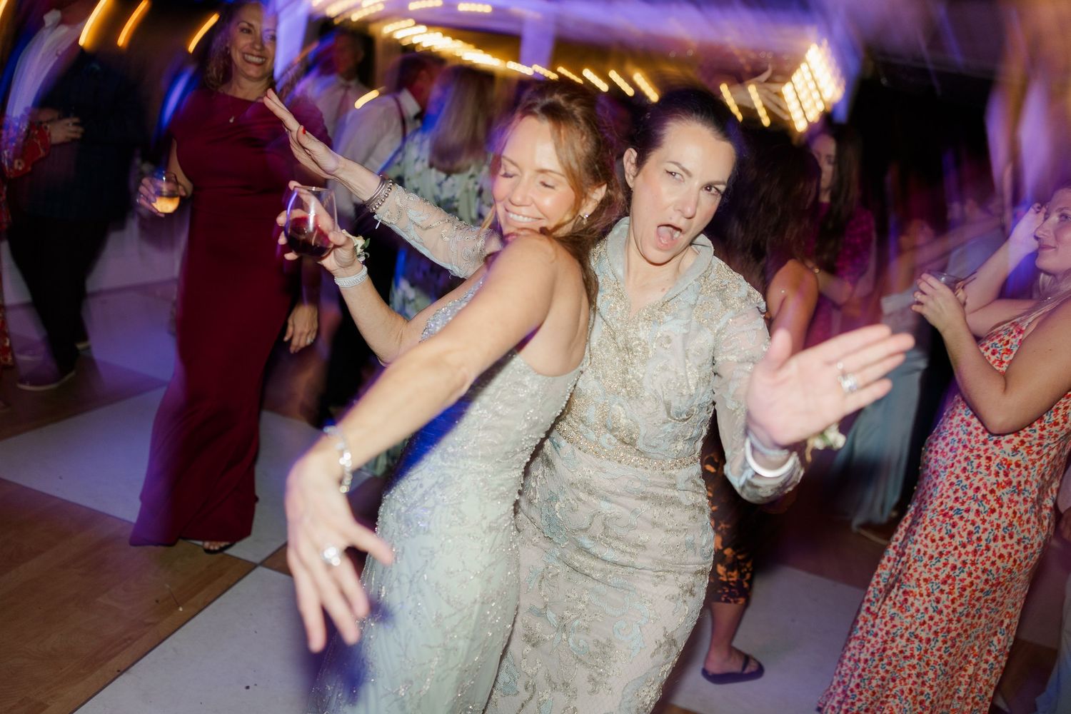 Wedding guests dancing enthusiastically at a reception with purple ambient lighting.