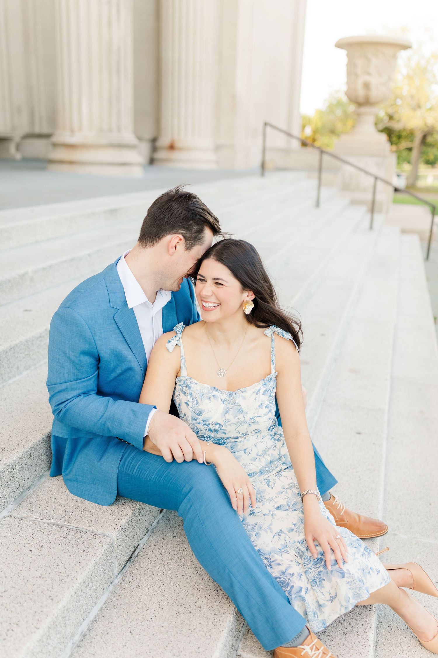 A couple dressed in blue sits intimately on outdoor stone steps during an engagement photoshoot.