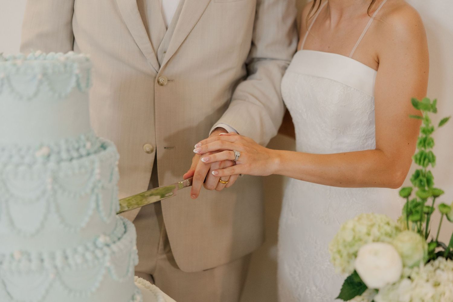 Bride and groom cut elegant three-tier light blue wedding cake together at their reception celebration.