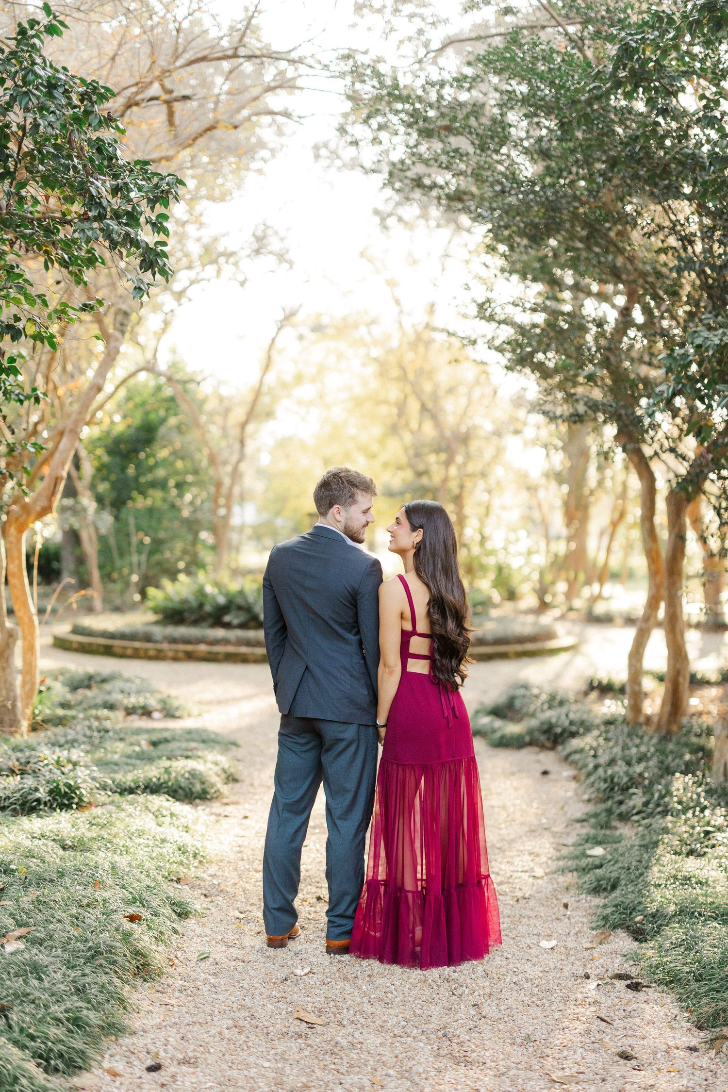 Couple walks hand in hand along garden path surrounded by lush greenery at sunset.
