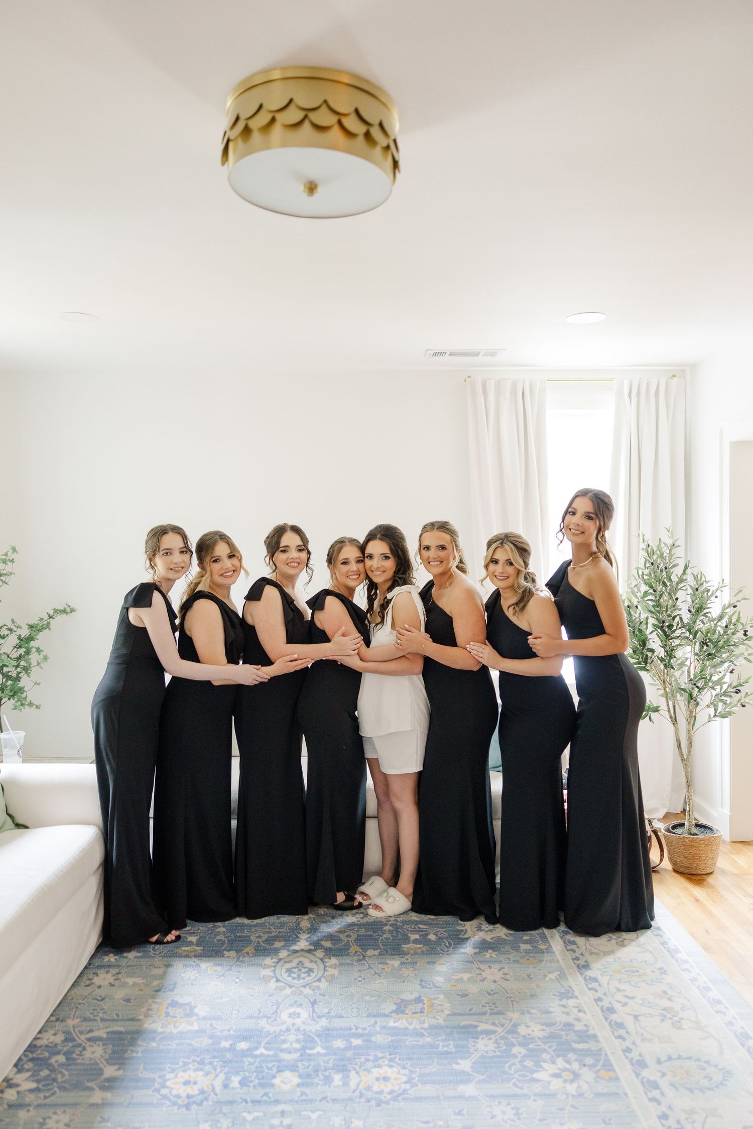 Wedding party wearing black dresses lined up in a bright white room with a creative pose.