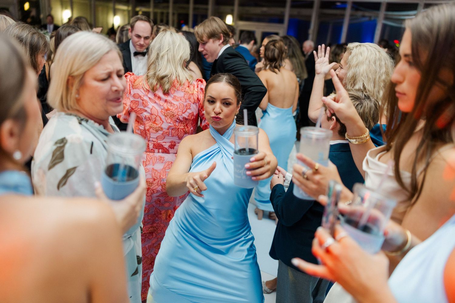 Wedding party and guests dancing energetically at reception with colorful lighting.