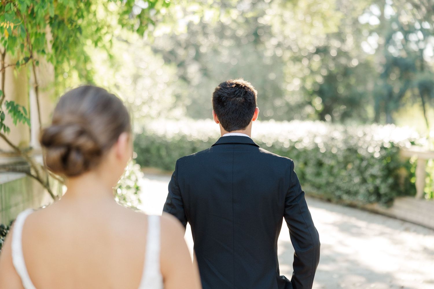 A bride and groom walk together on a tree-lined path during their outdoor wedding celebration.