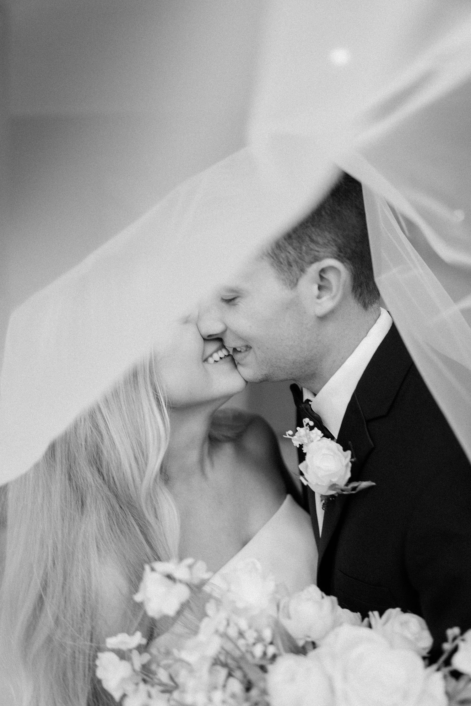 Romantic black and white portrait of wedding couple under flowing veil.