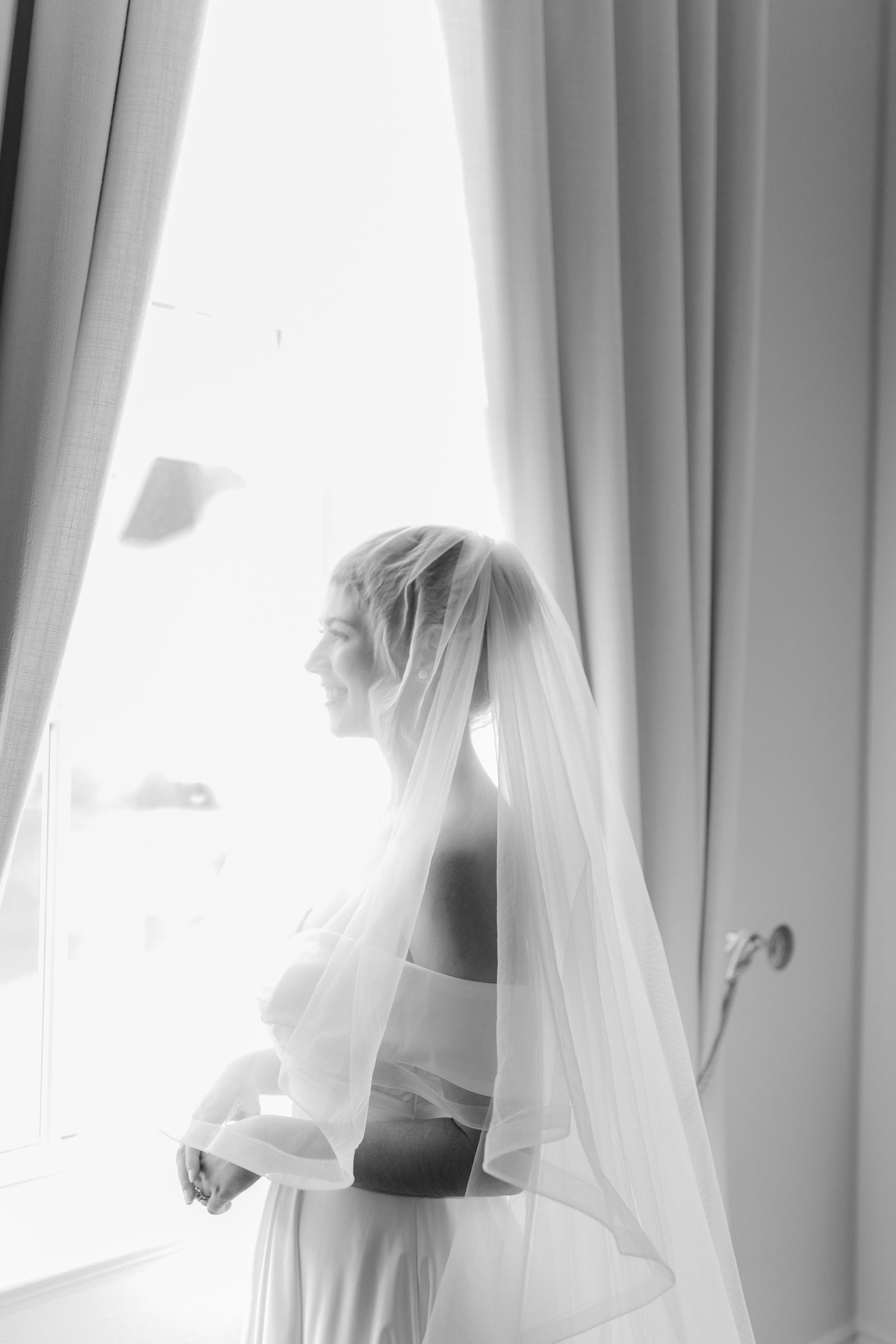 Ethereal black and white photo of bride in front of window with flowing veil.