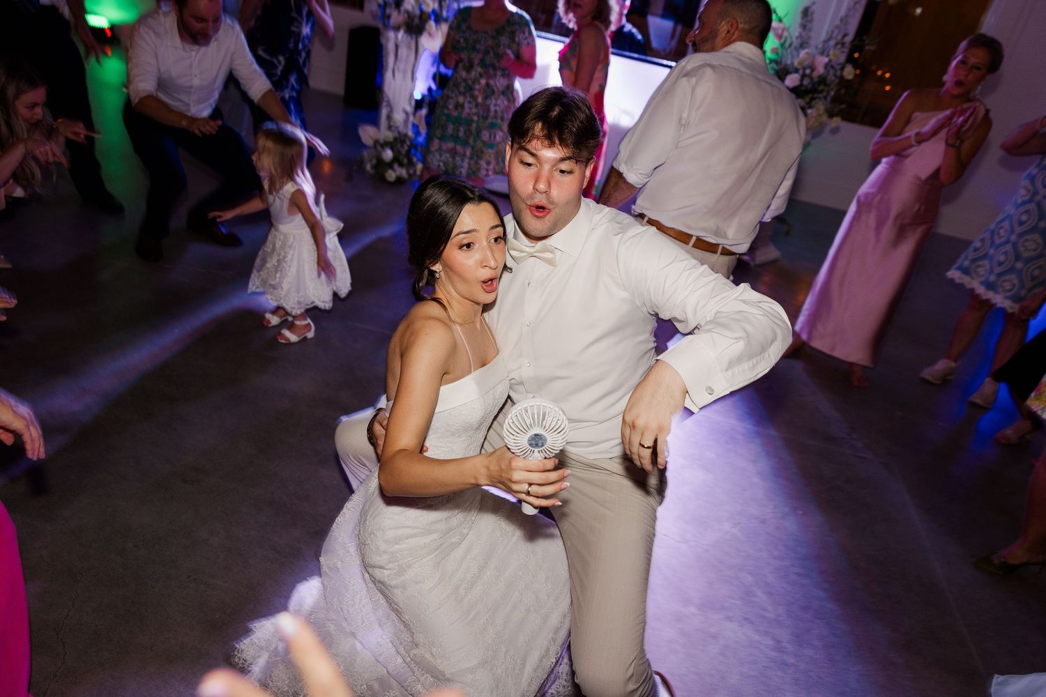 Bride and groom dancing energetically together on the wedding reception dance floor surrounded by guests.