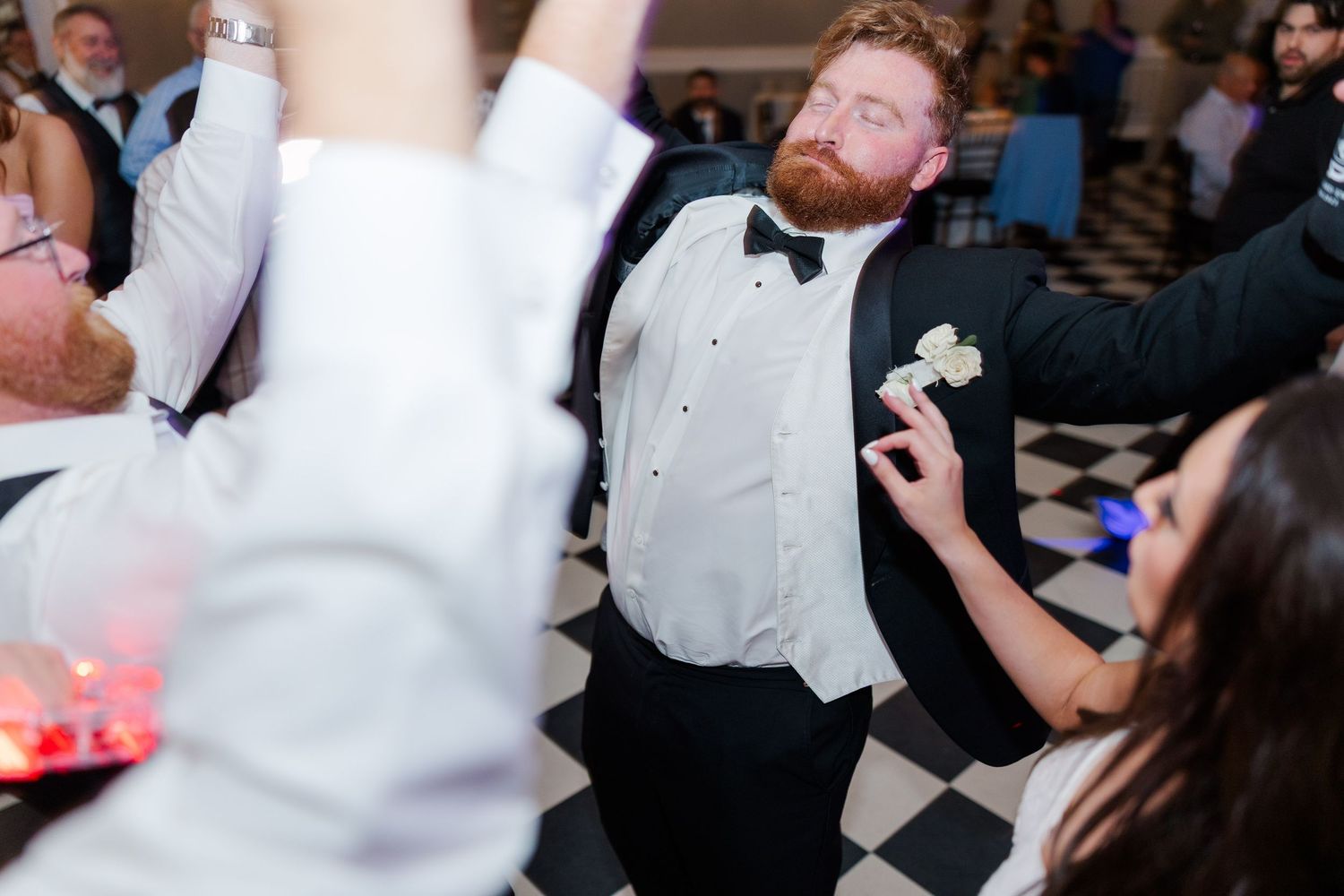 A wedding guest in formal attire dances energetically on a checkered ballroom floor.
