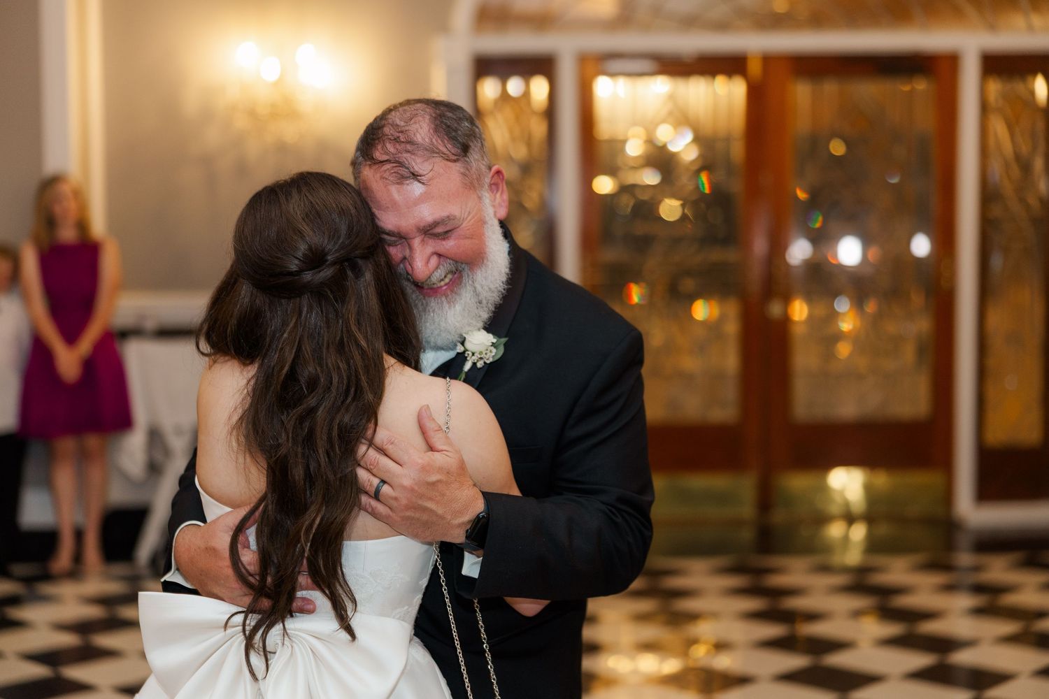 Father-daughter dance at wedding reception in warmly lit ballroom with chandeliers.
