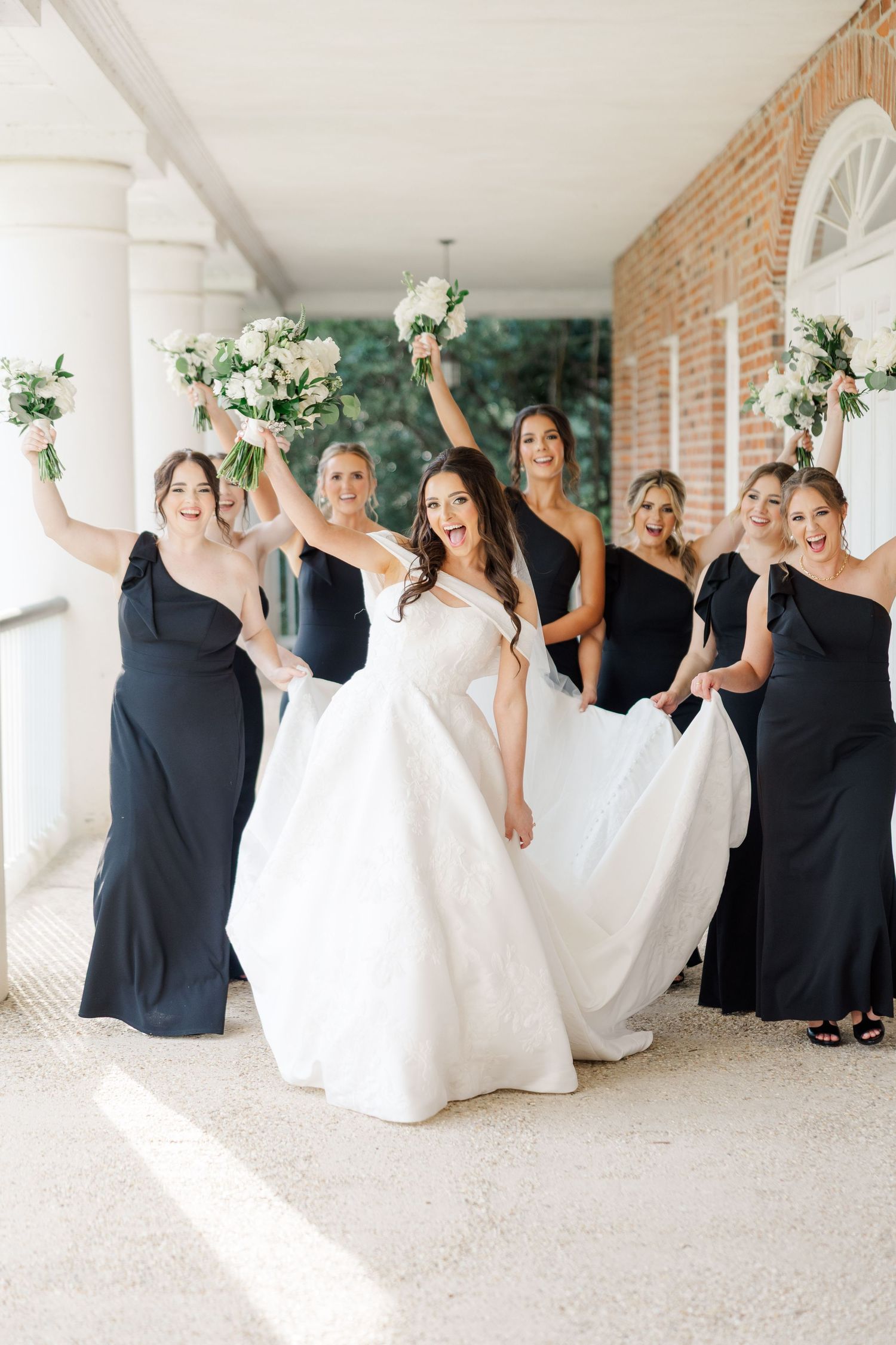 Bridal party in black and white dresses posing together on columned porch.