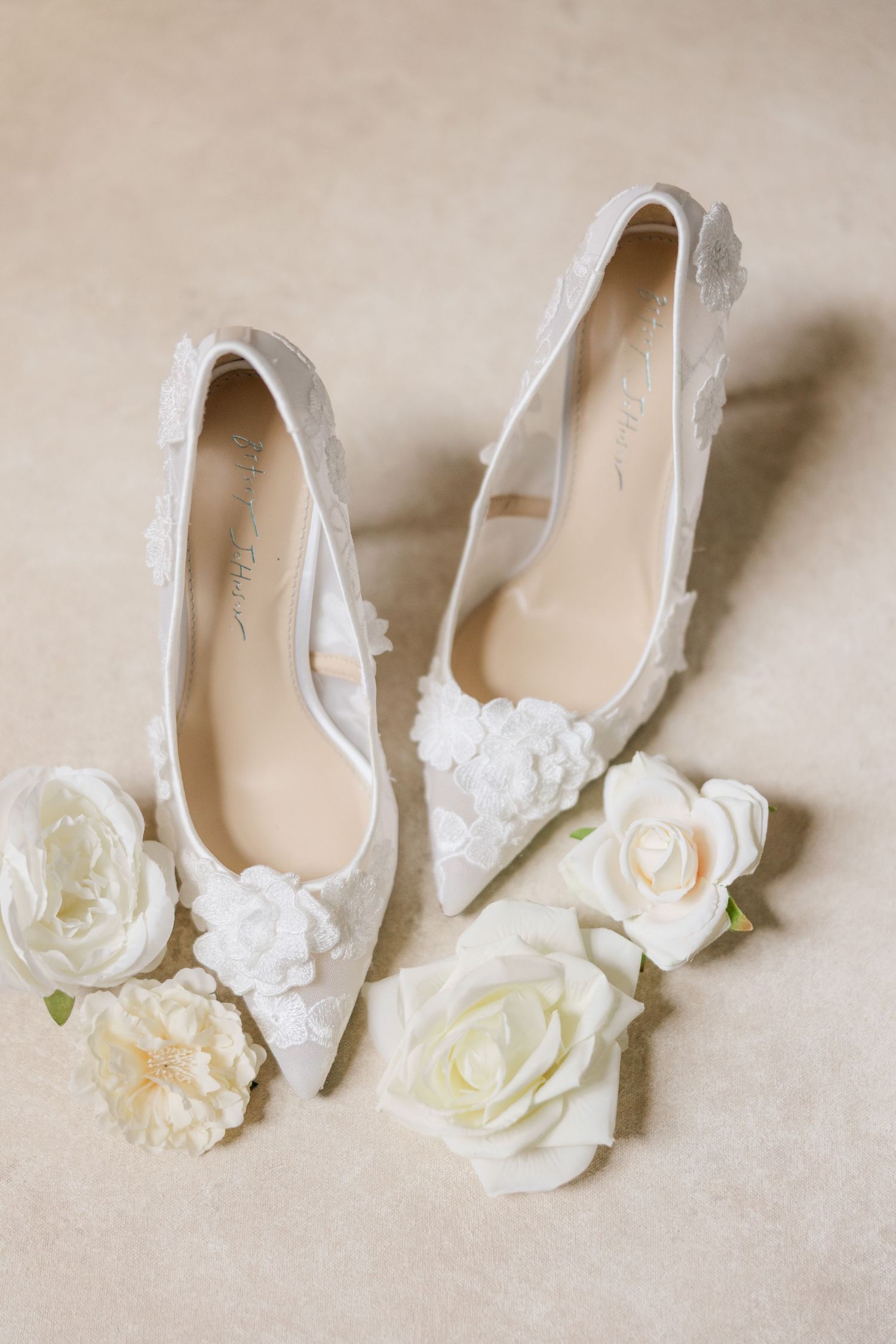 White wedding ballet flats with delicate floral embellishments arranged in a row against a neutral background.