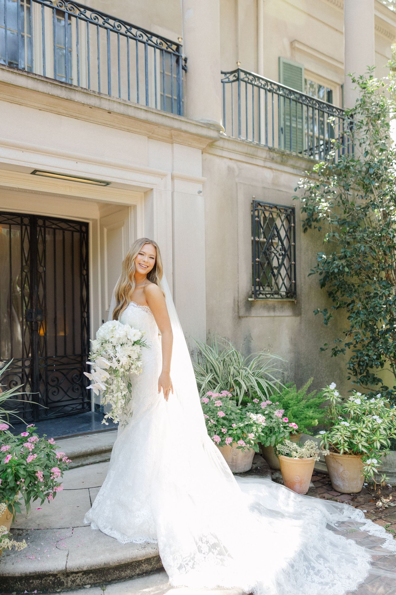 Beautiful wedding dress with cascading bouquet photographed on ornate mansion entrance steps.