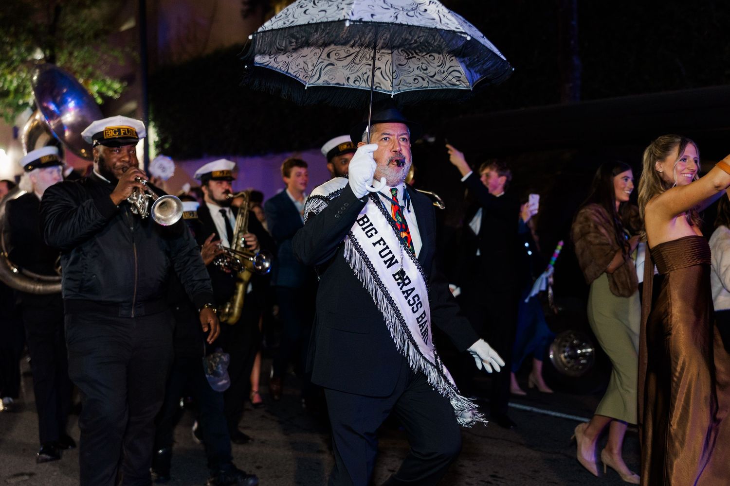 Wedding party gathered outside at night holding umbrellas with twinkling lights in background.