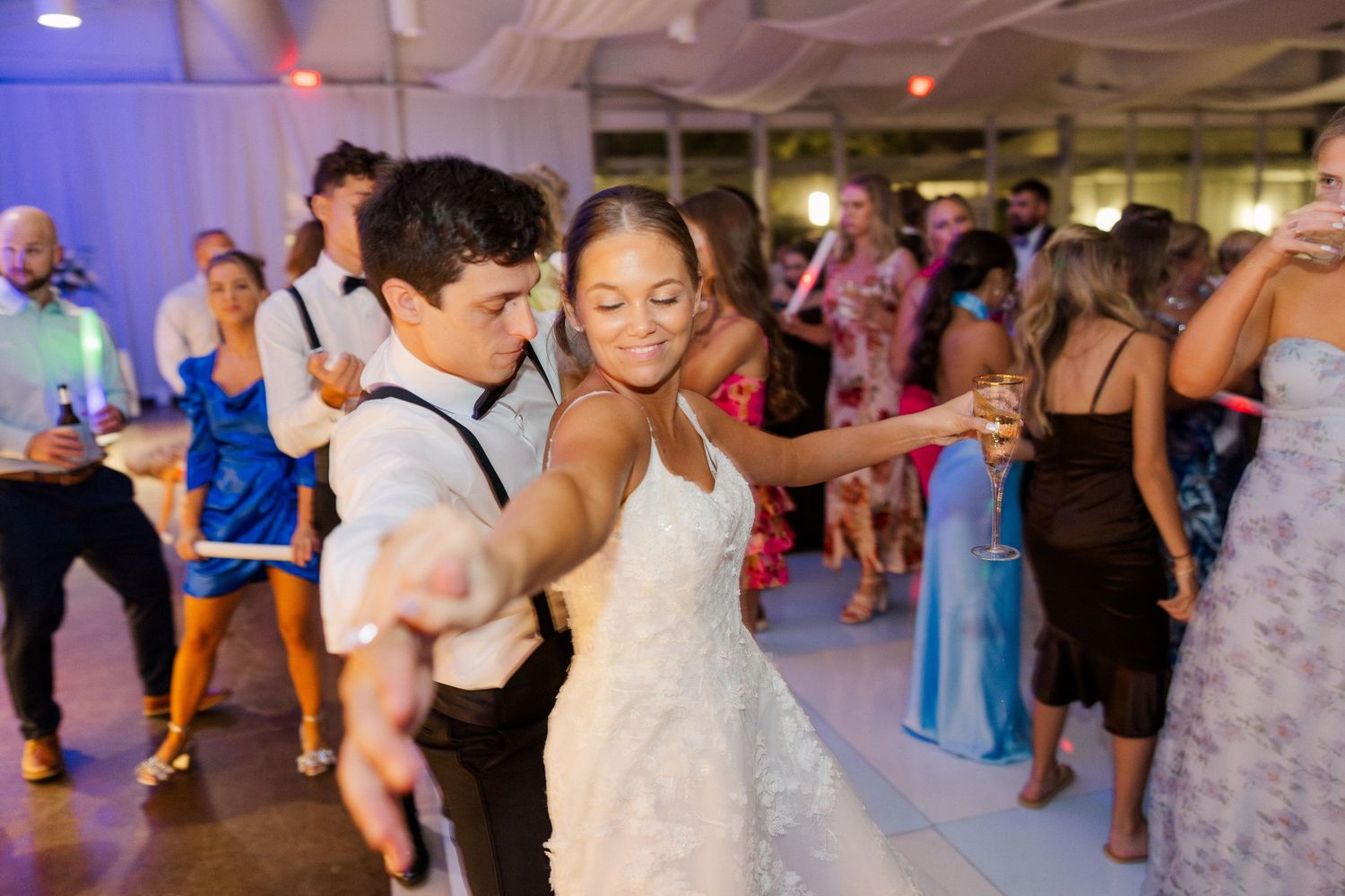 Guests dancing and celebrating at an indoor wedding reception with blue lighting and white decor.