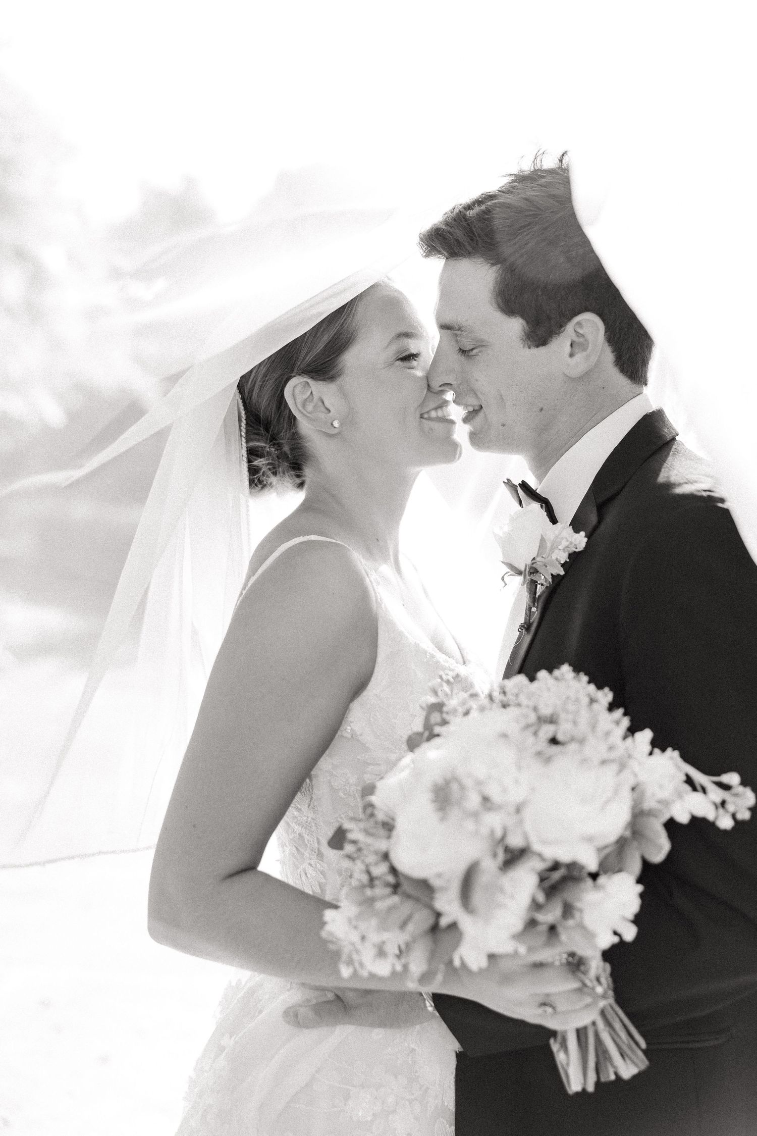 Black and white portrait of a couple sharing an intimate moment with white floral bouquet.