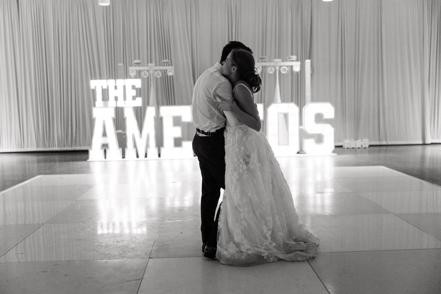 Black and white wedding photo with illuminated marquee letters in the background.