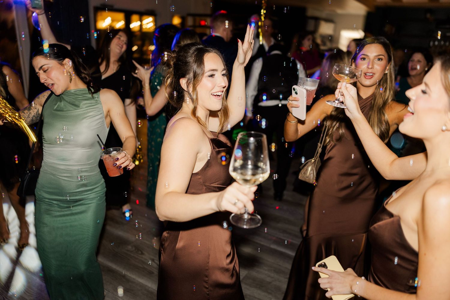 Wedding reception guests dancing and celebrating on a dimly lit dance floor.