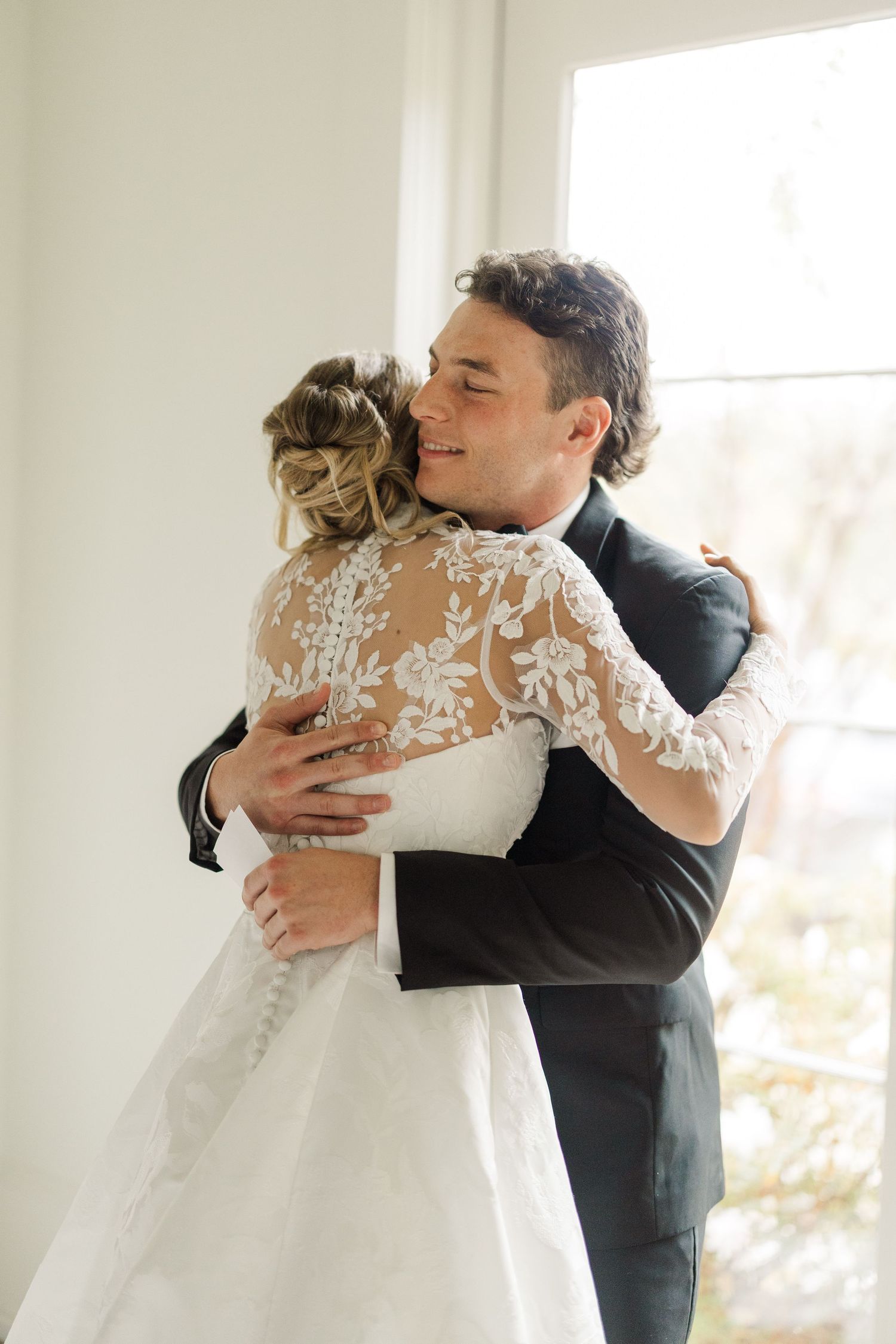 An emotional embrace between newlyweds during their first look in a sun-filled room.