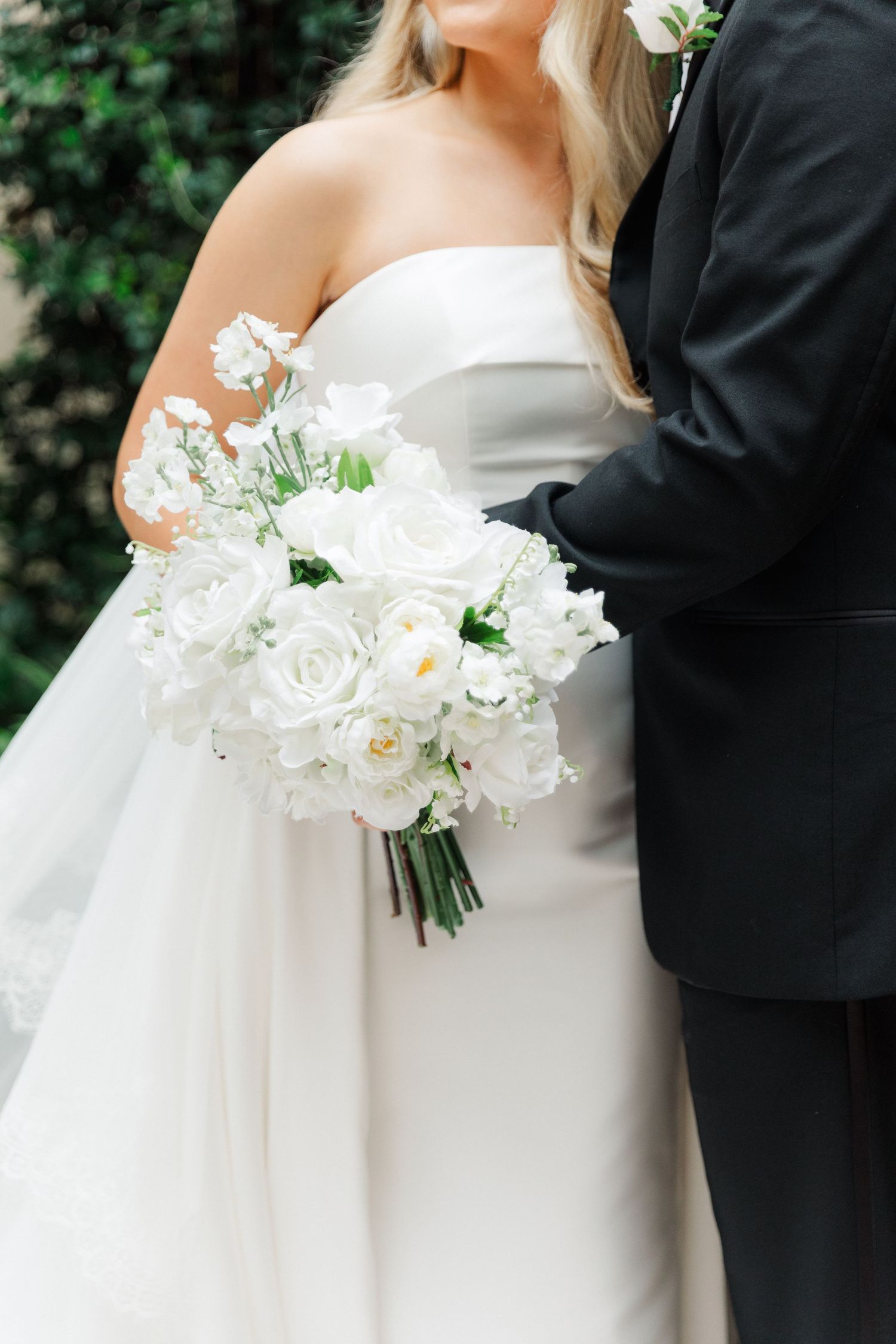 Close-up of bride holding elegant white rose bouquet next to groom in formal attire.