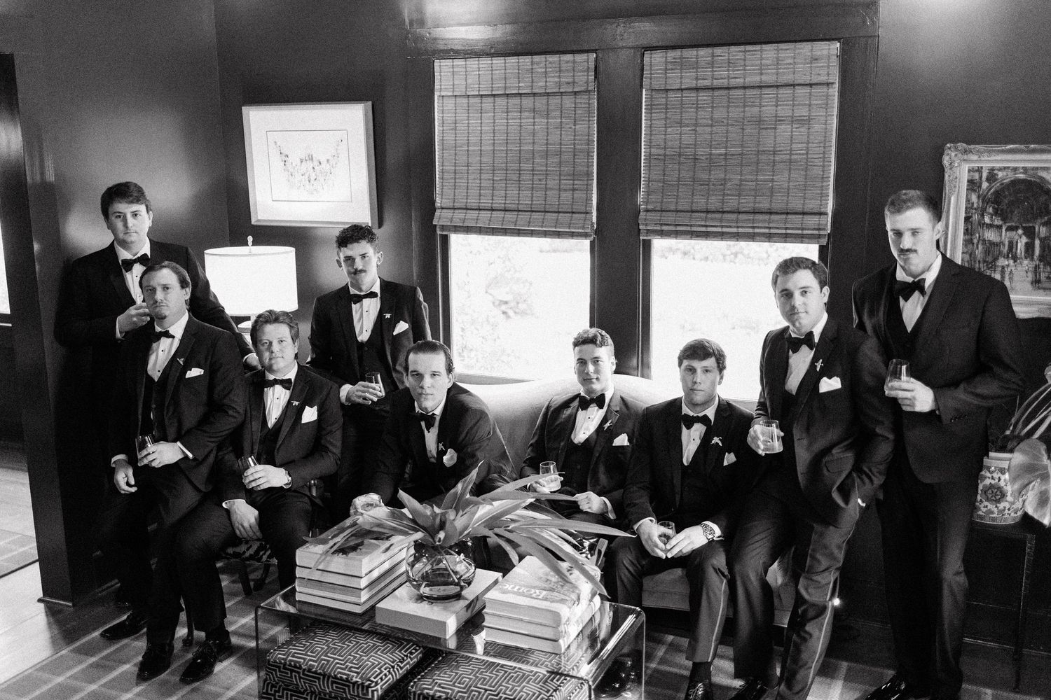 A vintage black and white photograph showing a group of formally dressed people gathered in a room with books and framed artwork.