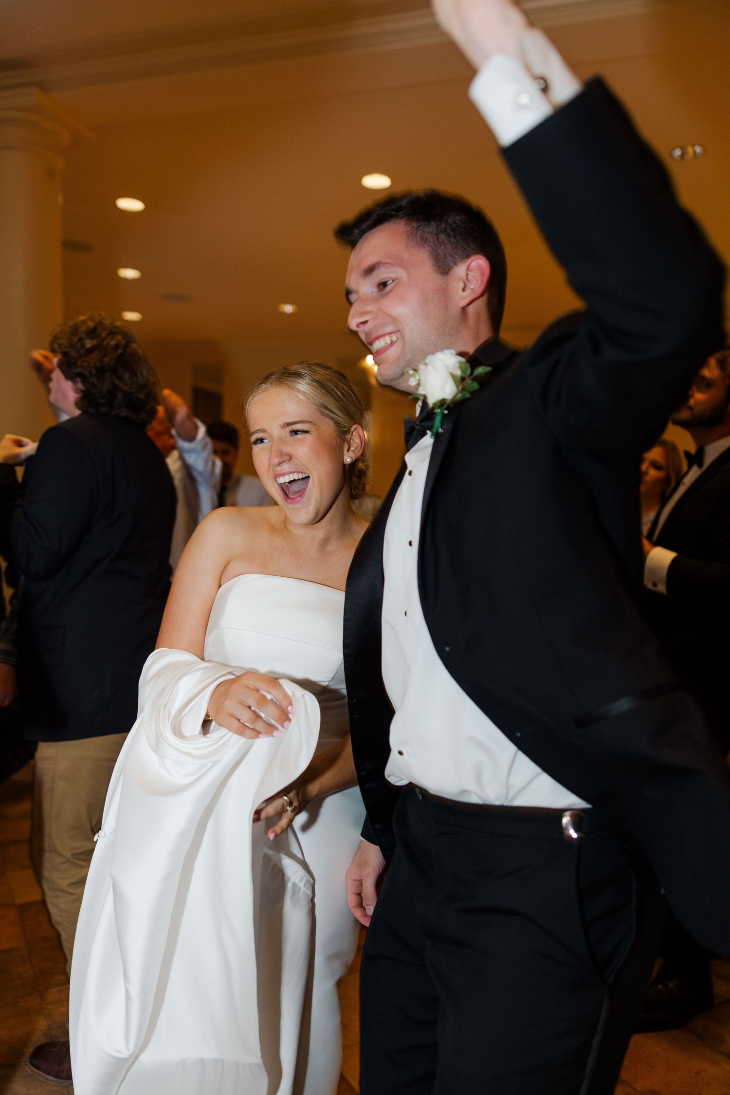 Wedding party members celebrate with joyful expressions and raised arms on the dance floor.