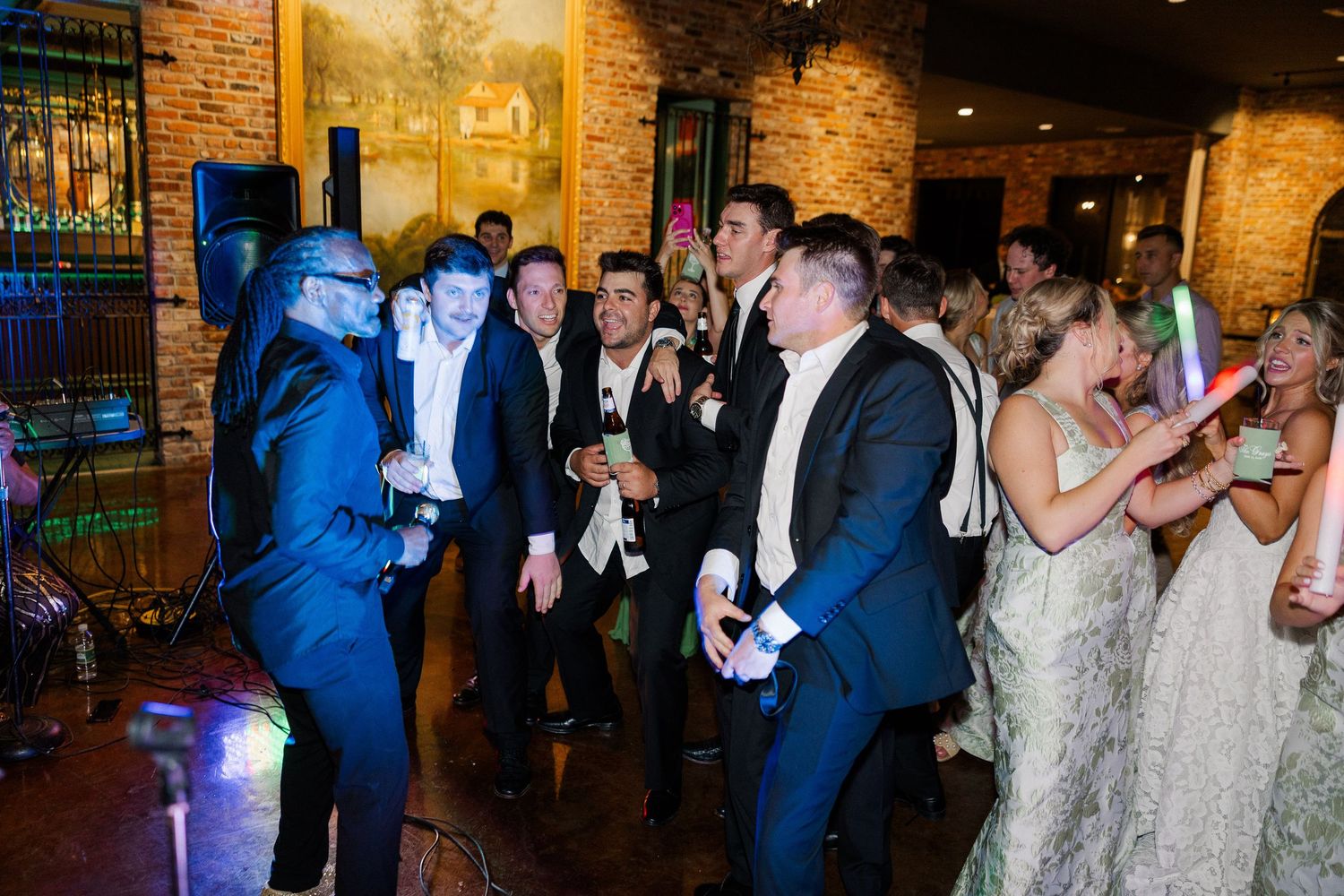 Energetic wedding reception dance floor with guests in formal attire celebrating with glow sticks and live music.