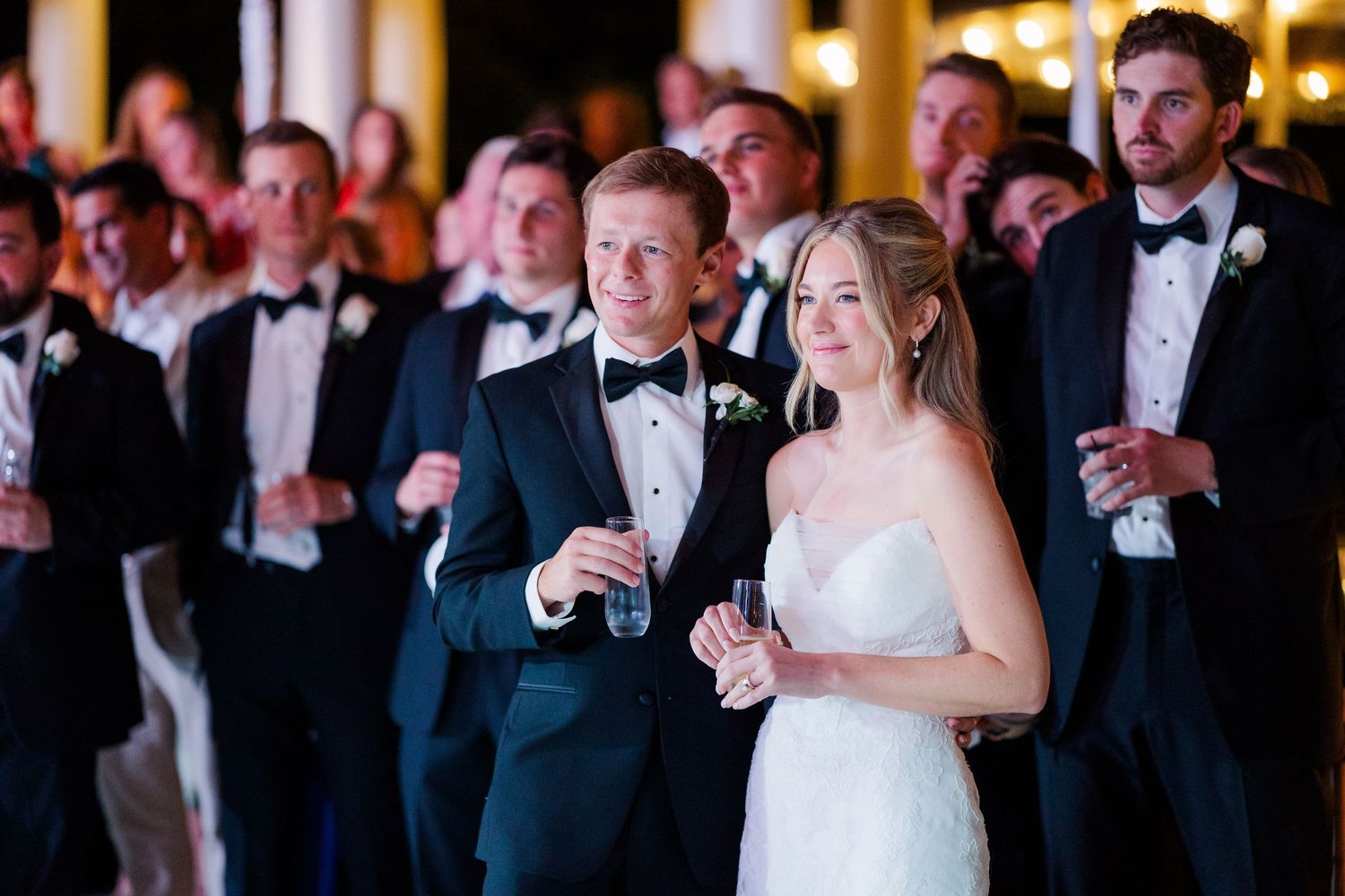 Wedding guests in formal attire celebrate during evening reception.