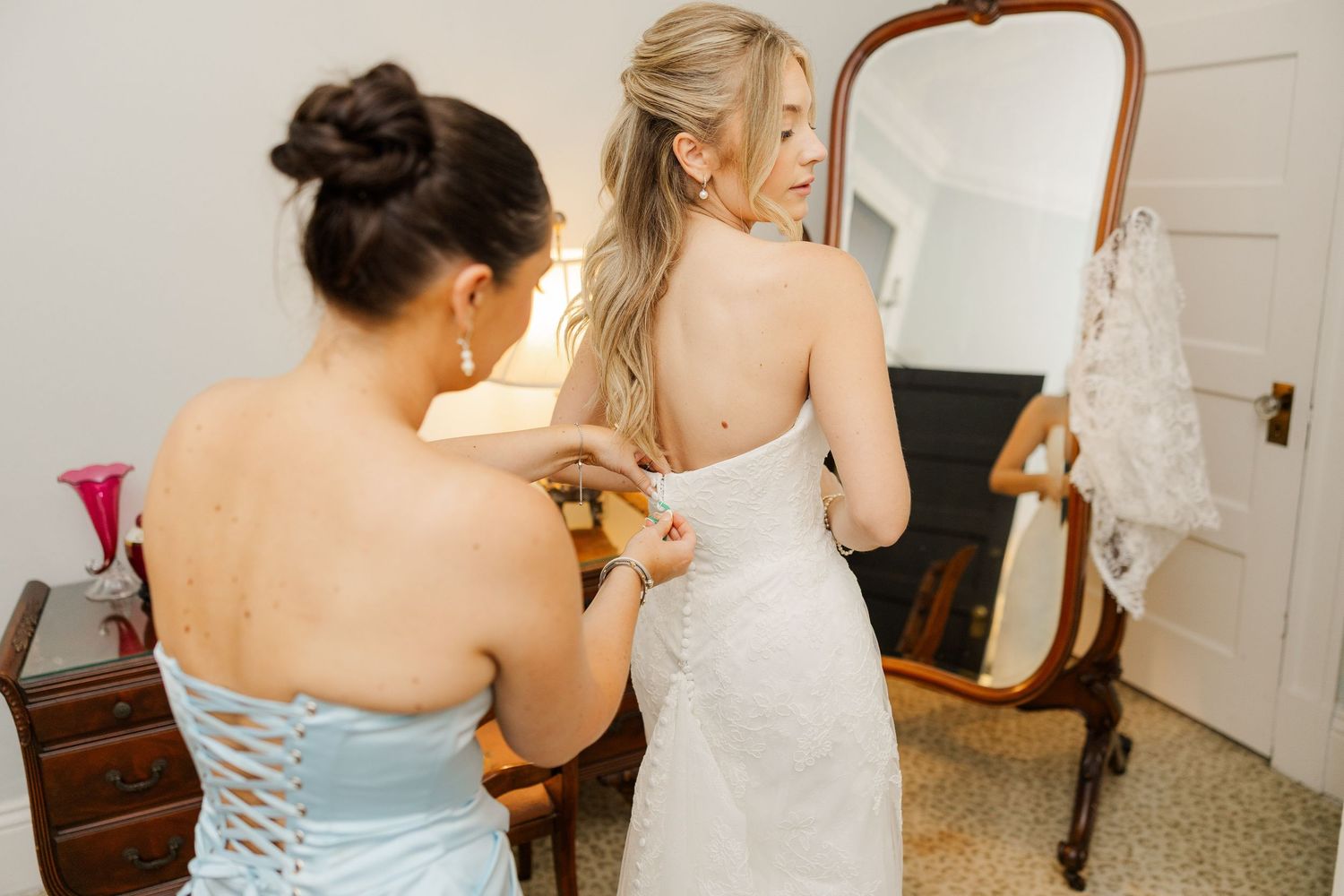 Bridesmaids in light blue dresses helping with wedding dress preparations.